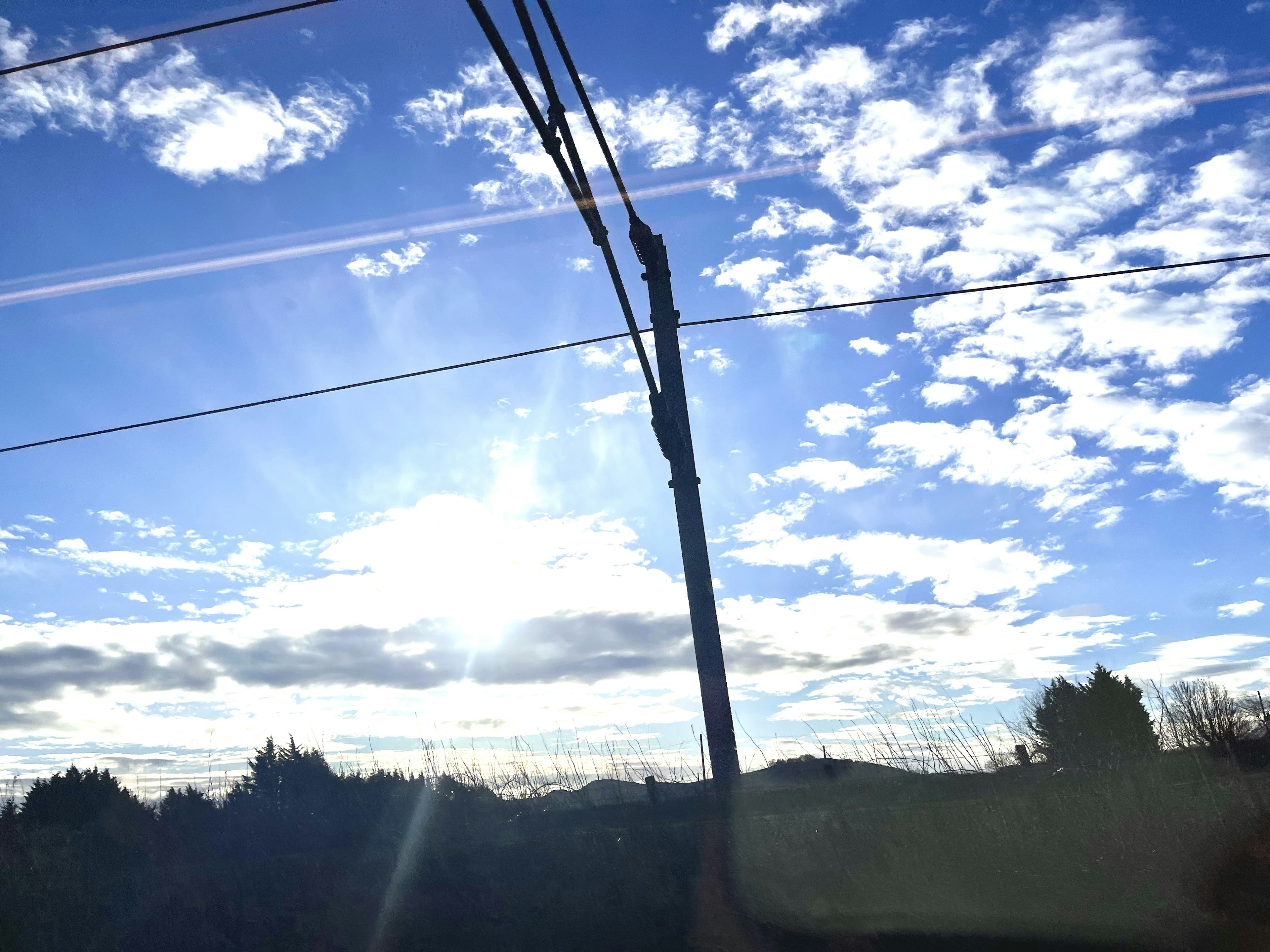 Un ciel bleu clair avec des nuages blancs et des lignes électriques au premier plan