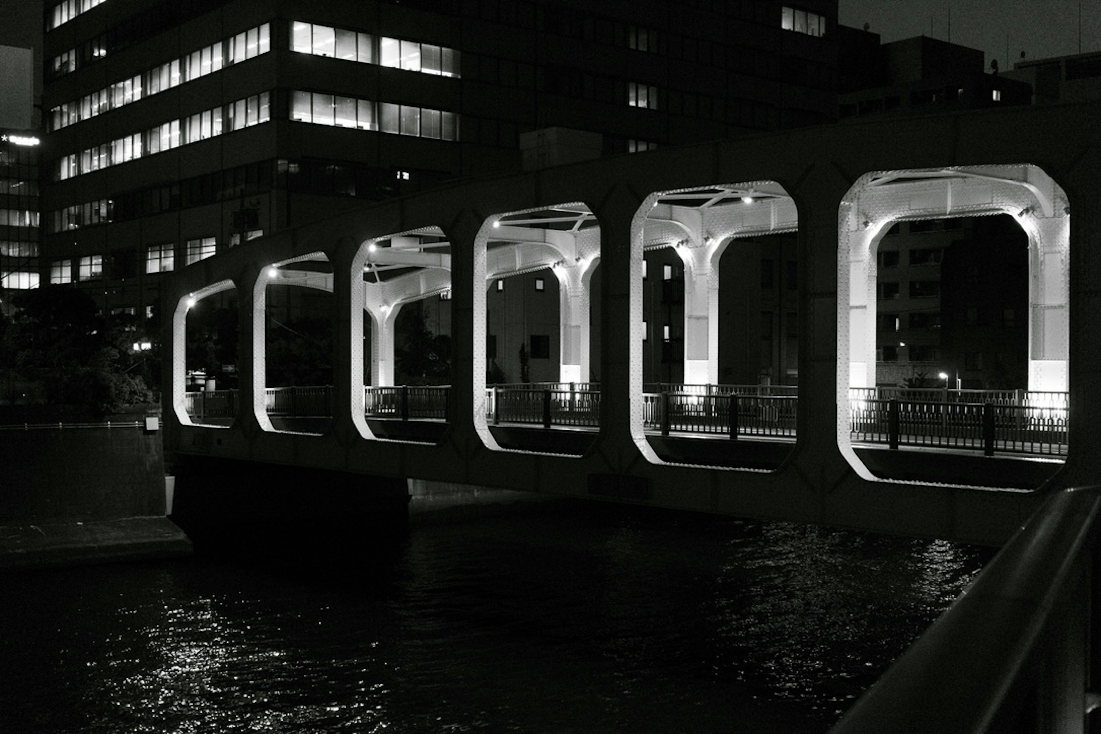 Foto en blanco y negro de un puente urbano por la noche con arcos y reflejos en el agua