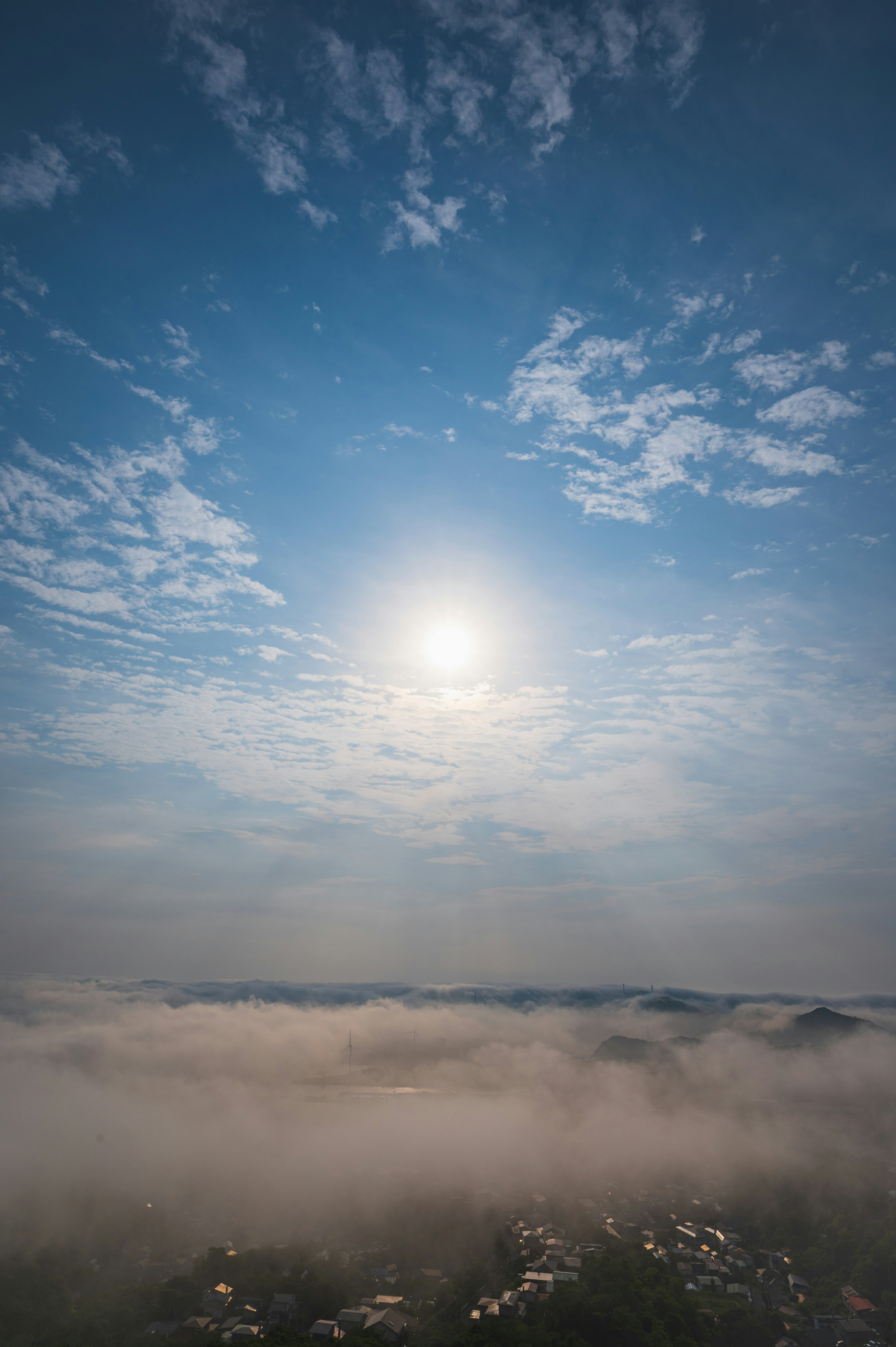 青空と雲に覆われた太陽と霧に包まれた山々の風景