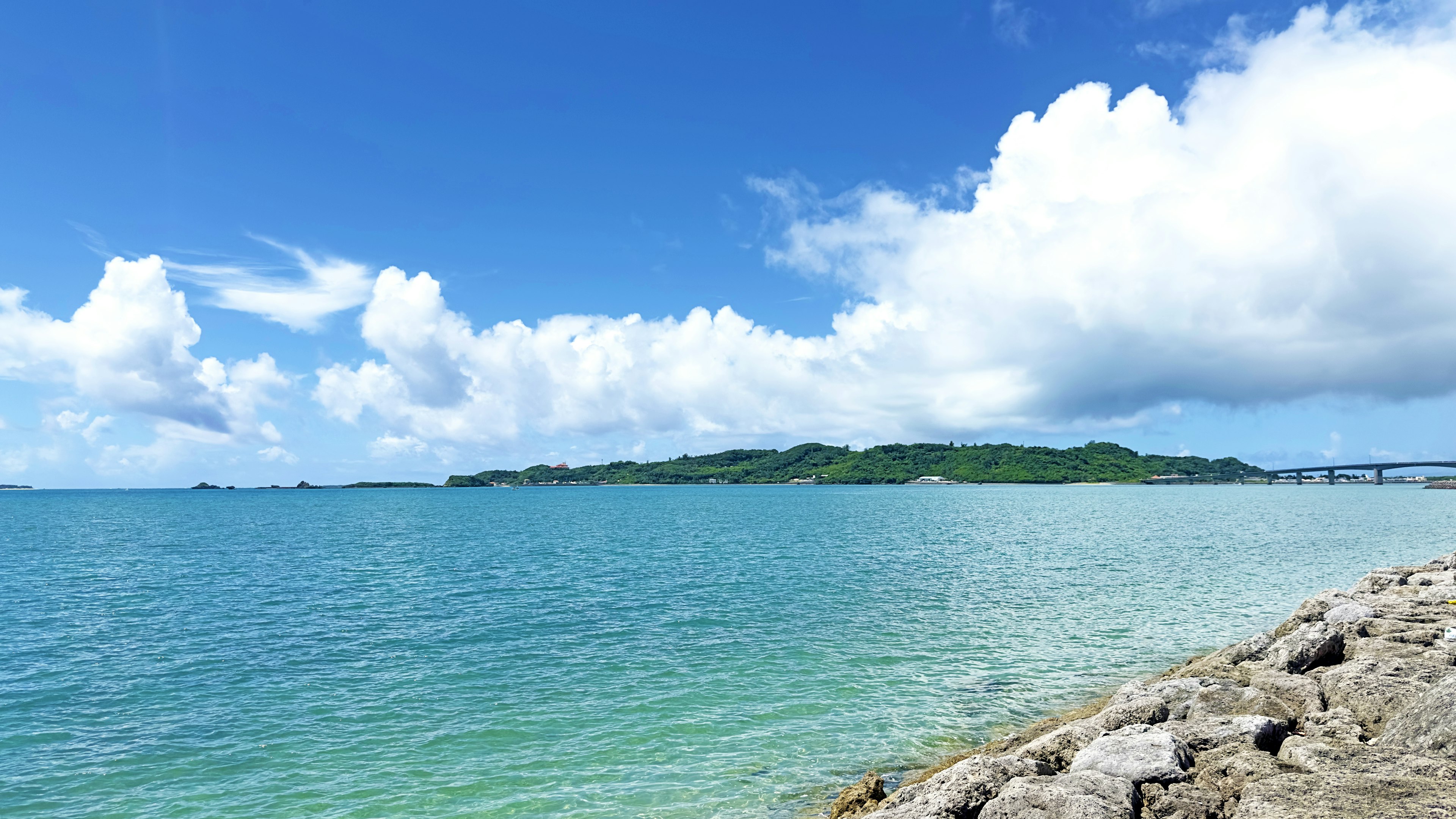 Scenic view of blue ocean and white clouds with visible bridge