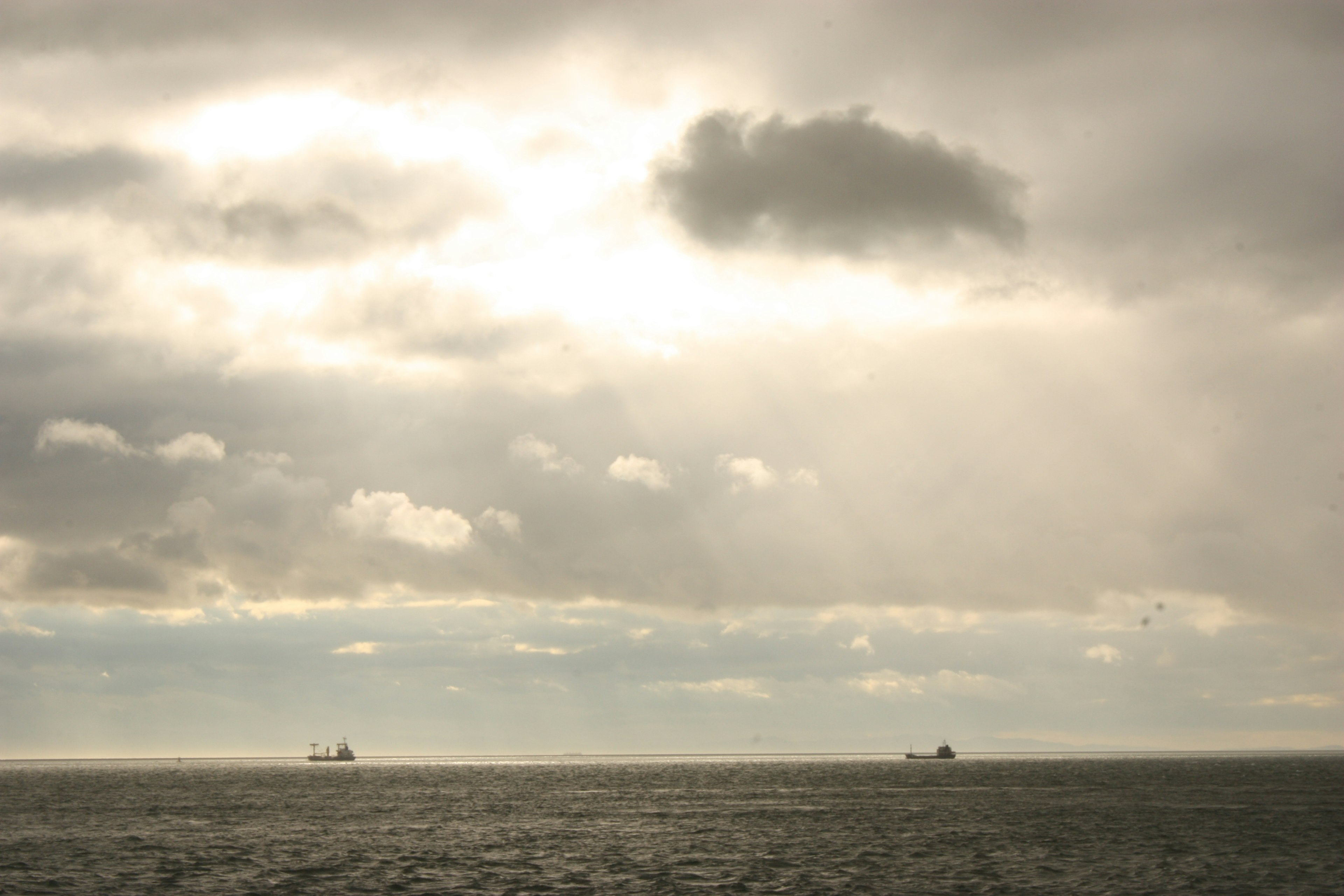 Dos barcos en el océano bajo un cielo nublado con rayos de luz