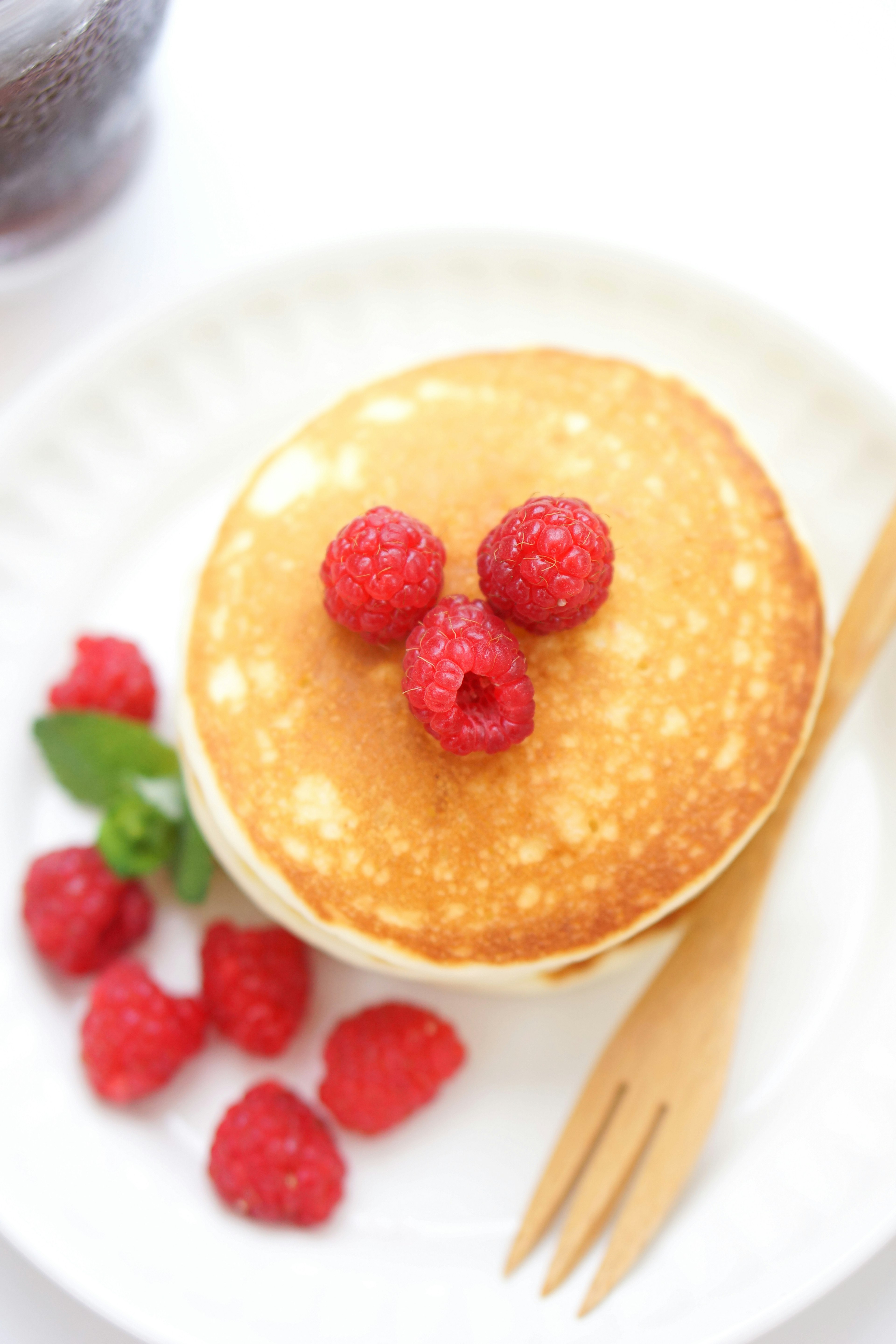 Assiette de pancakes surmontés de framboises disposées de manière ludique