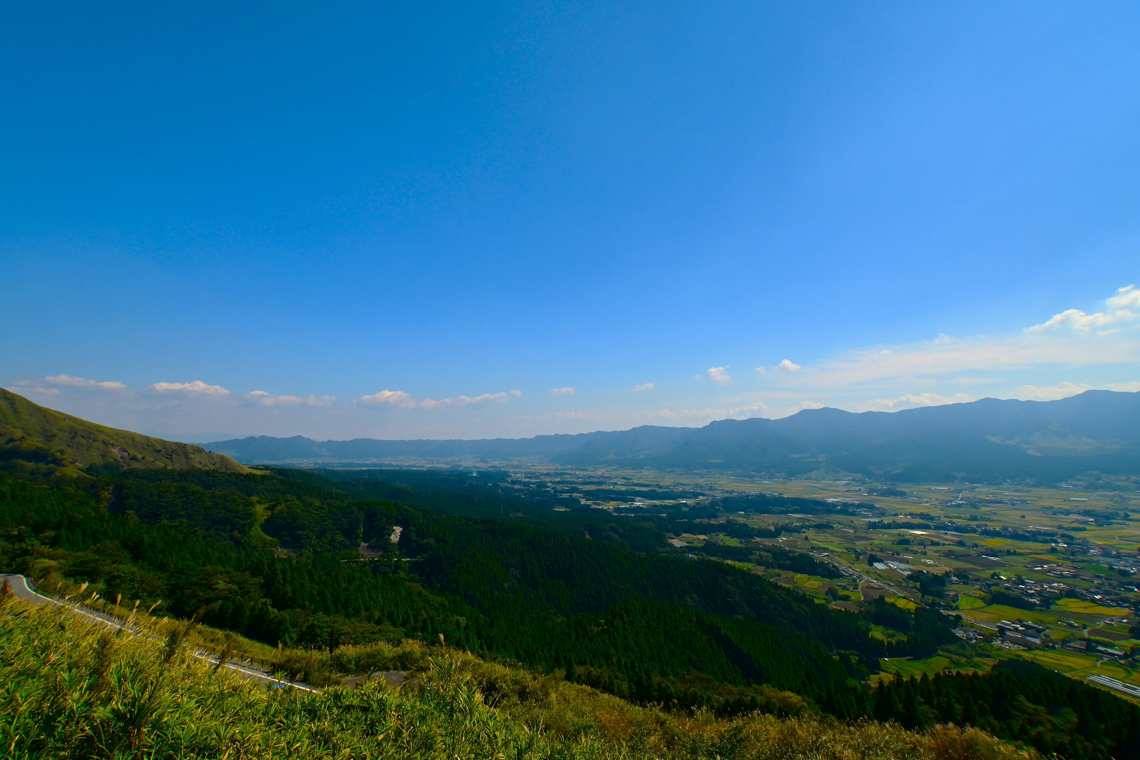 青空の下、山々と広がる谷の風景が見える