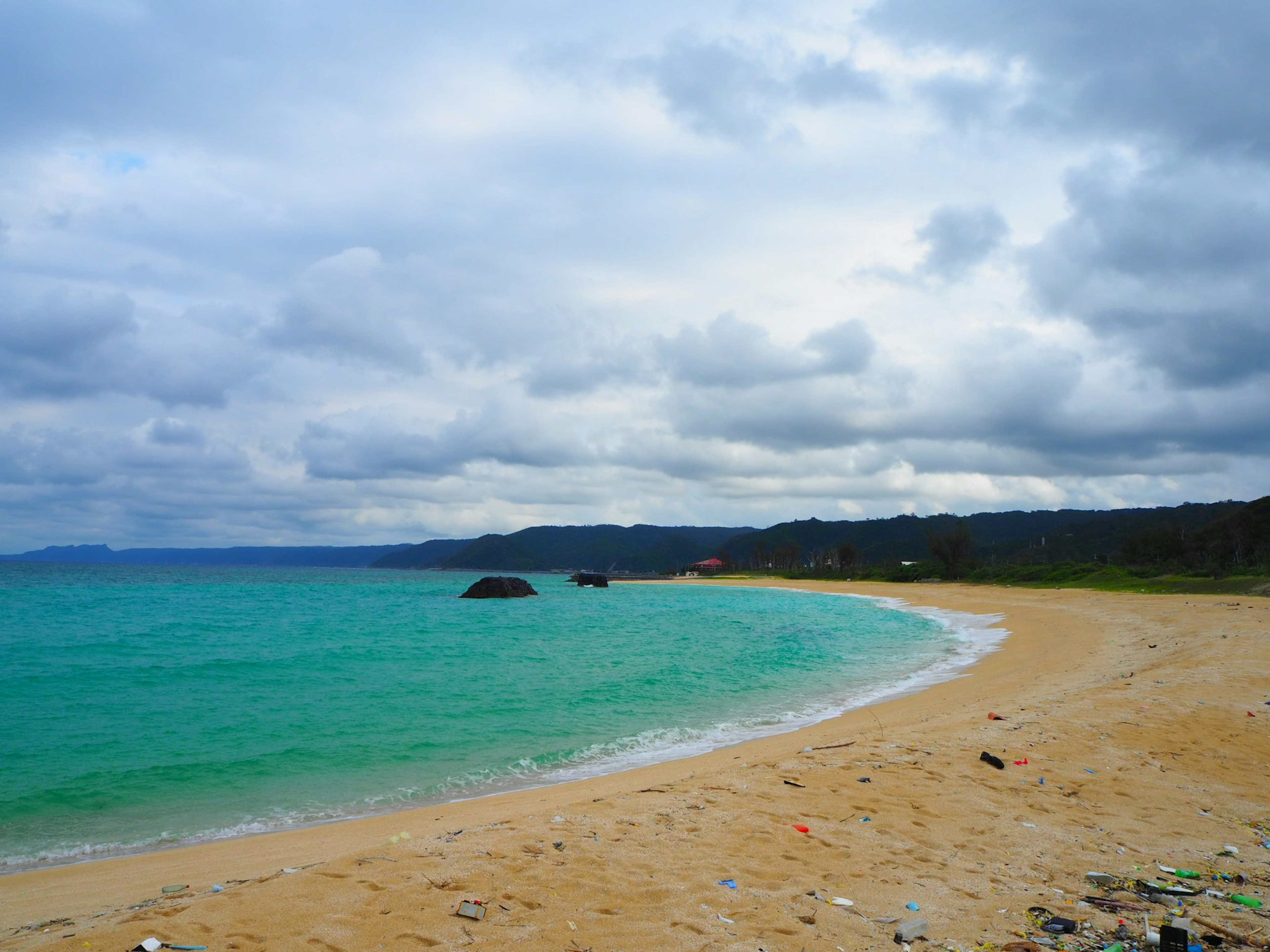 Pemandangan pantai berpasir dengan air turquoise dan langit mendung