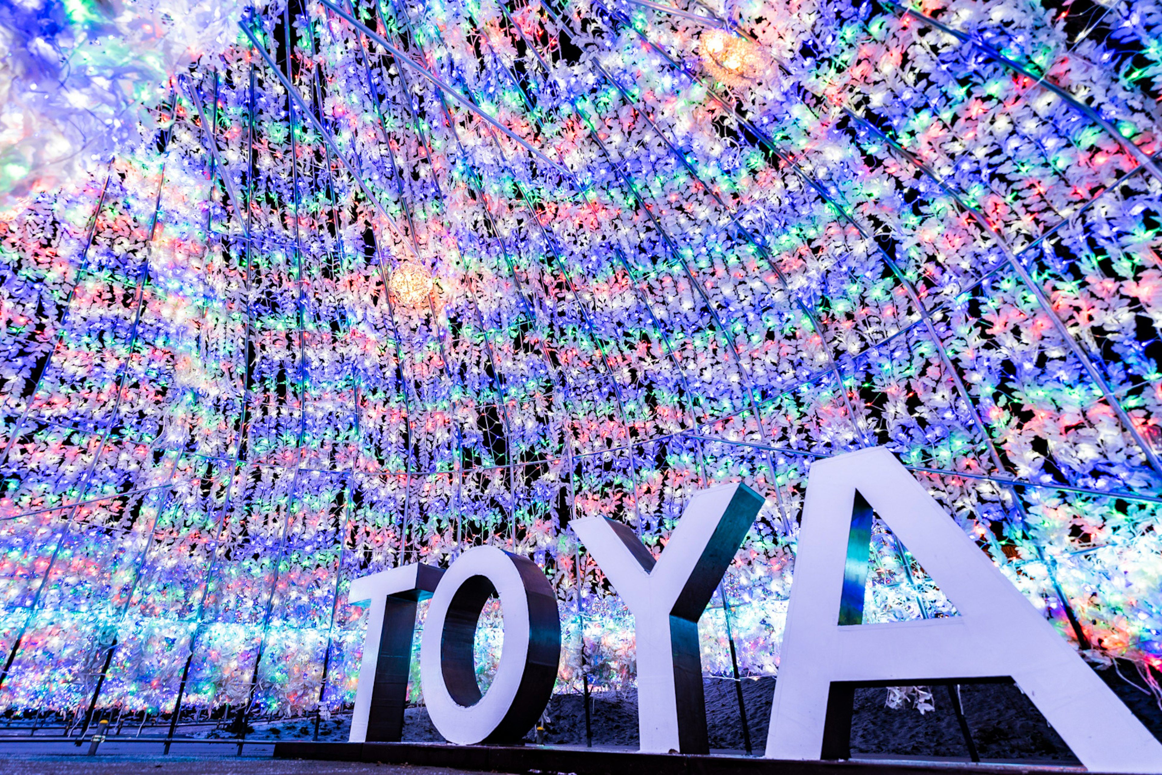 Large letters spelling 'TOYA' in front of a colorful illuminated backdrop