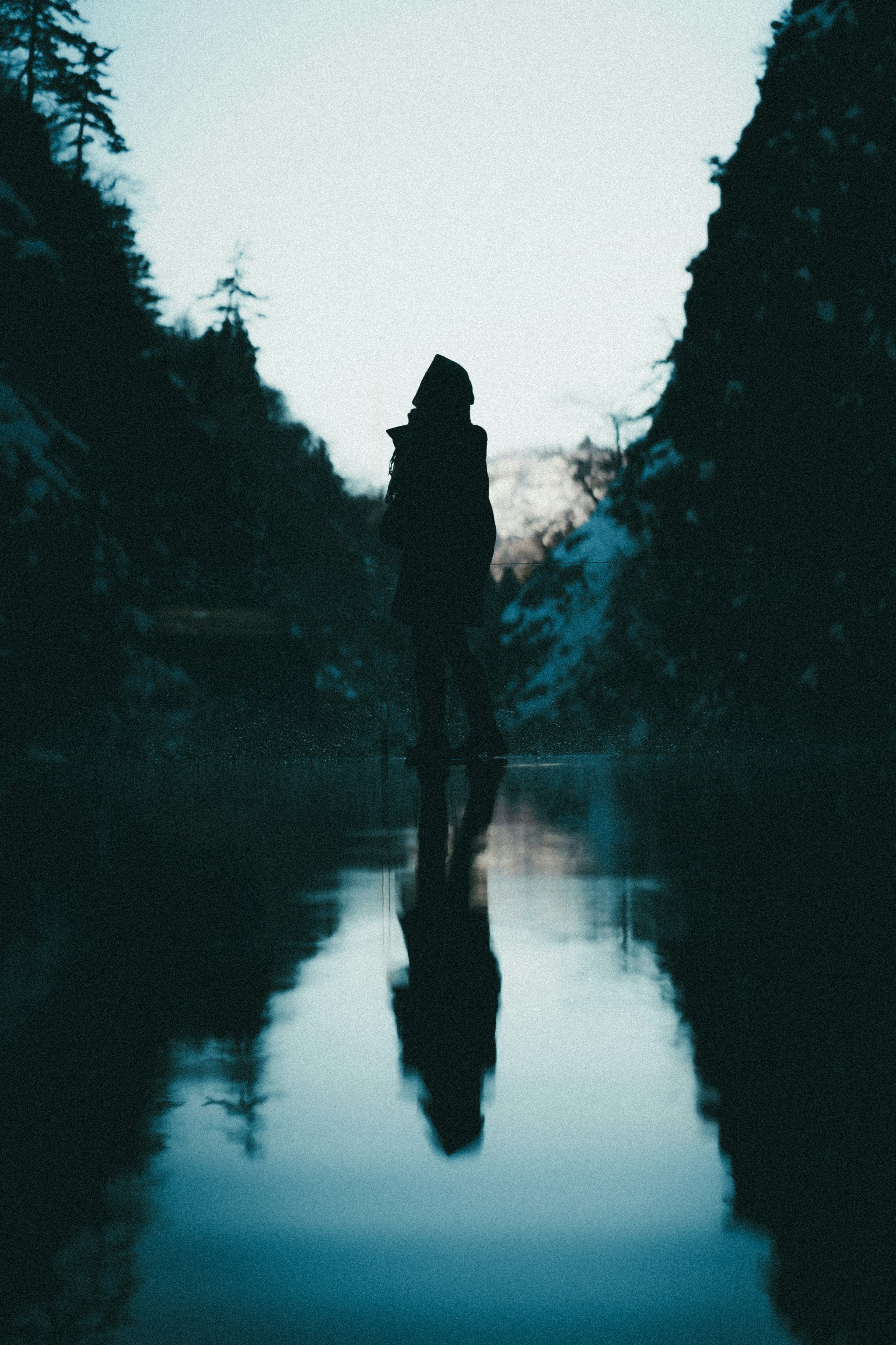 Silhouette di una persona in piedi su un lago calmo che riflette la natura circostante