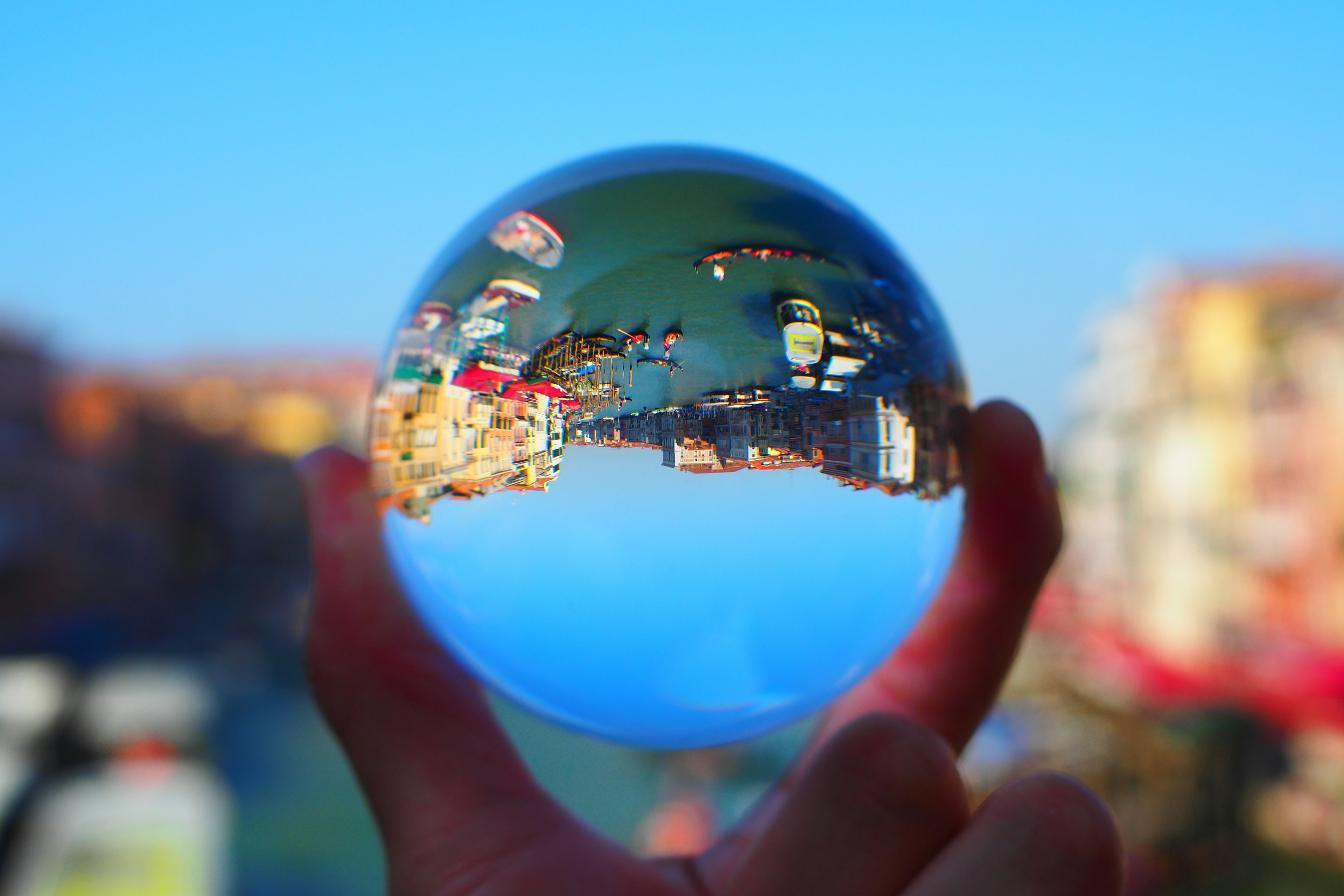 Una bola de cristal clara sostenida en la mano que refleja una escena junto al agua