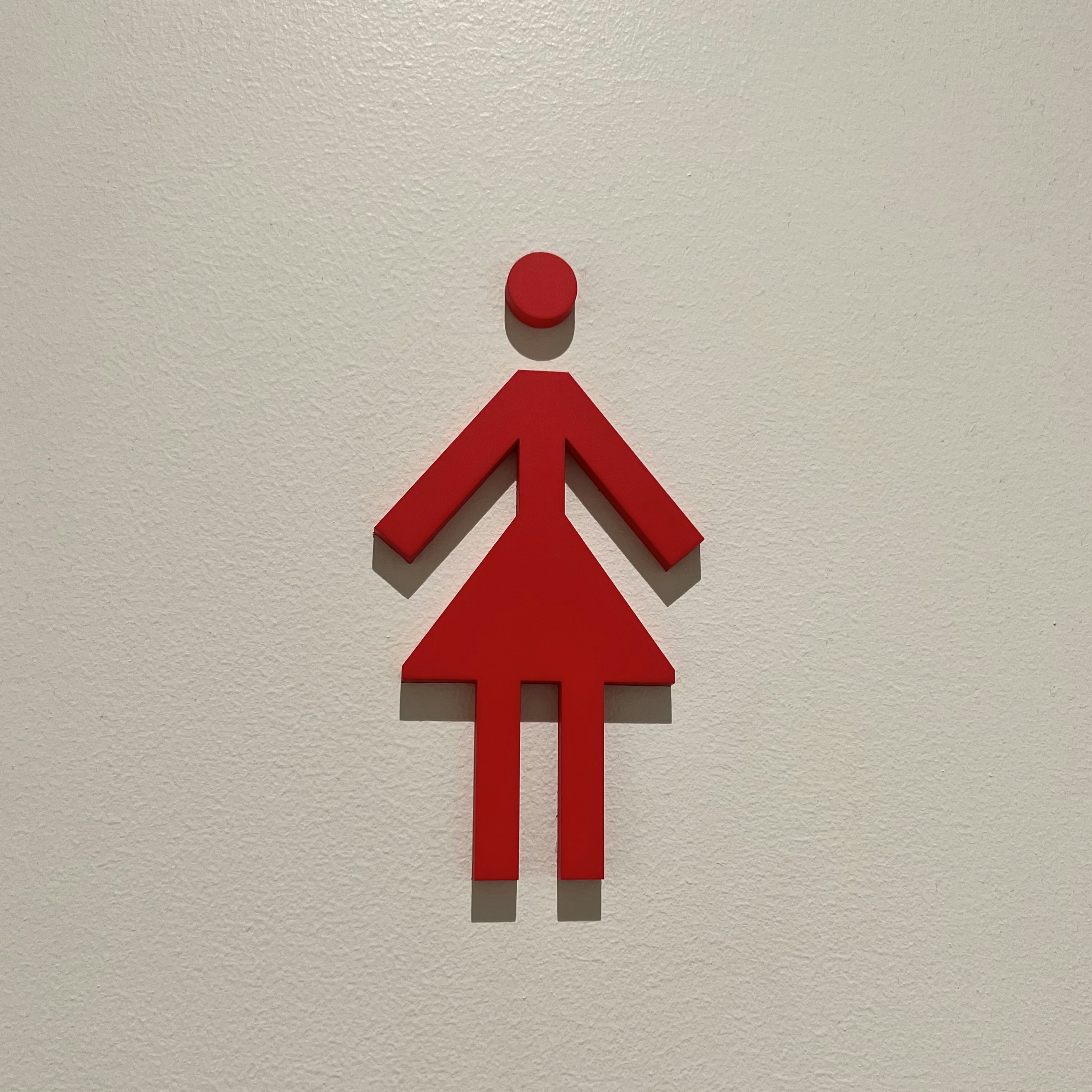 Segnale di bagno femminile rosso montato su un muro bianco