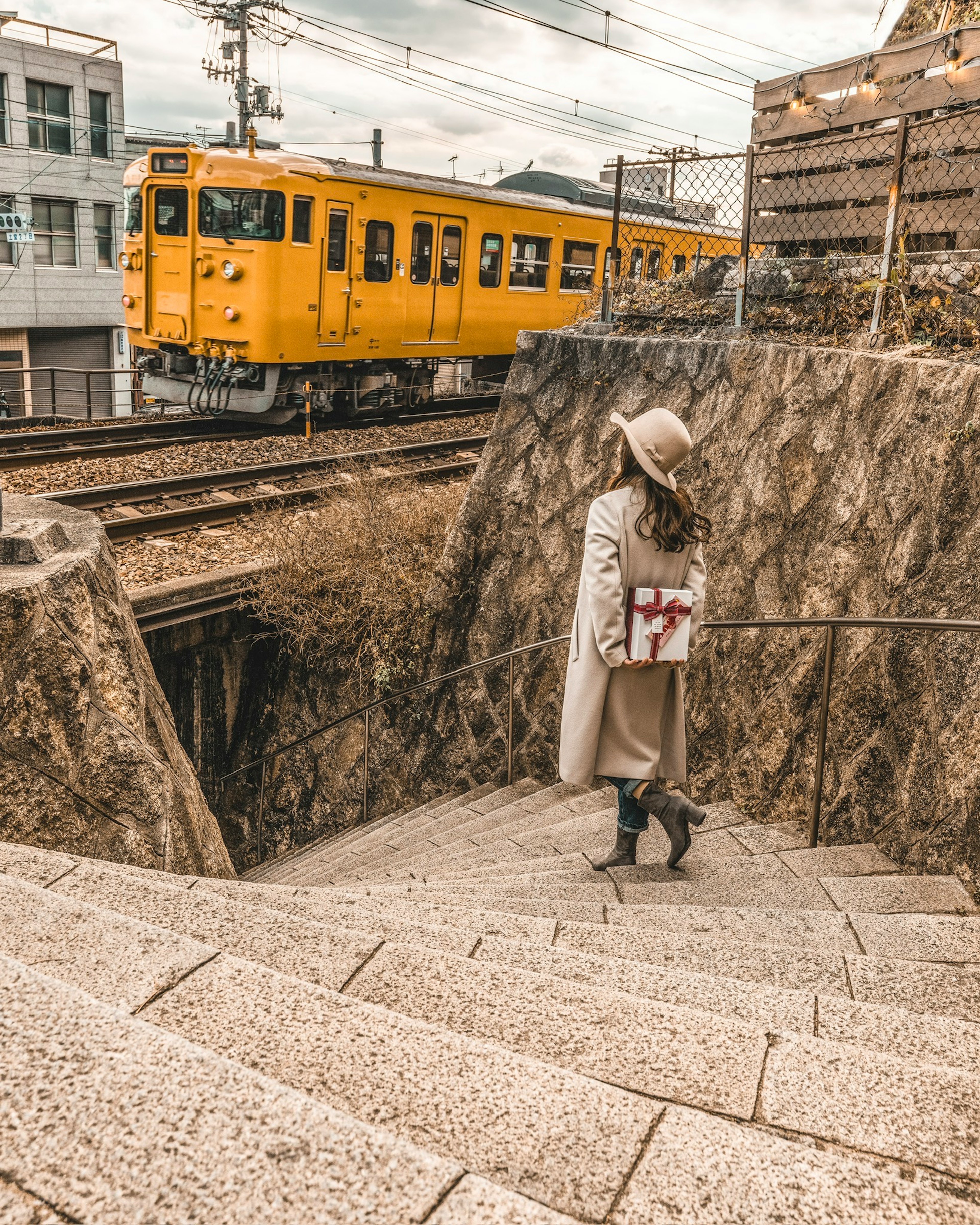 Woman standing on stone stairs with a yellow train in the background