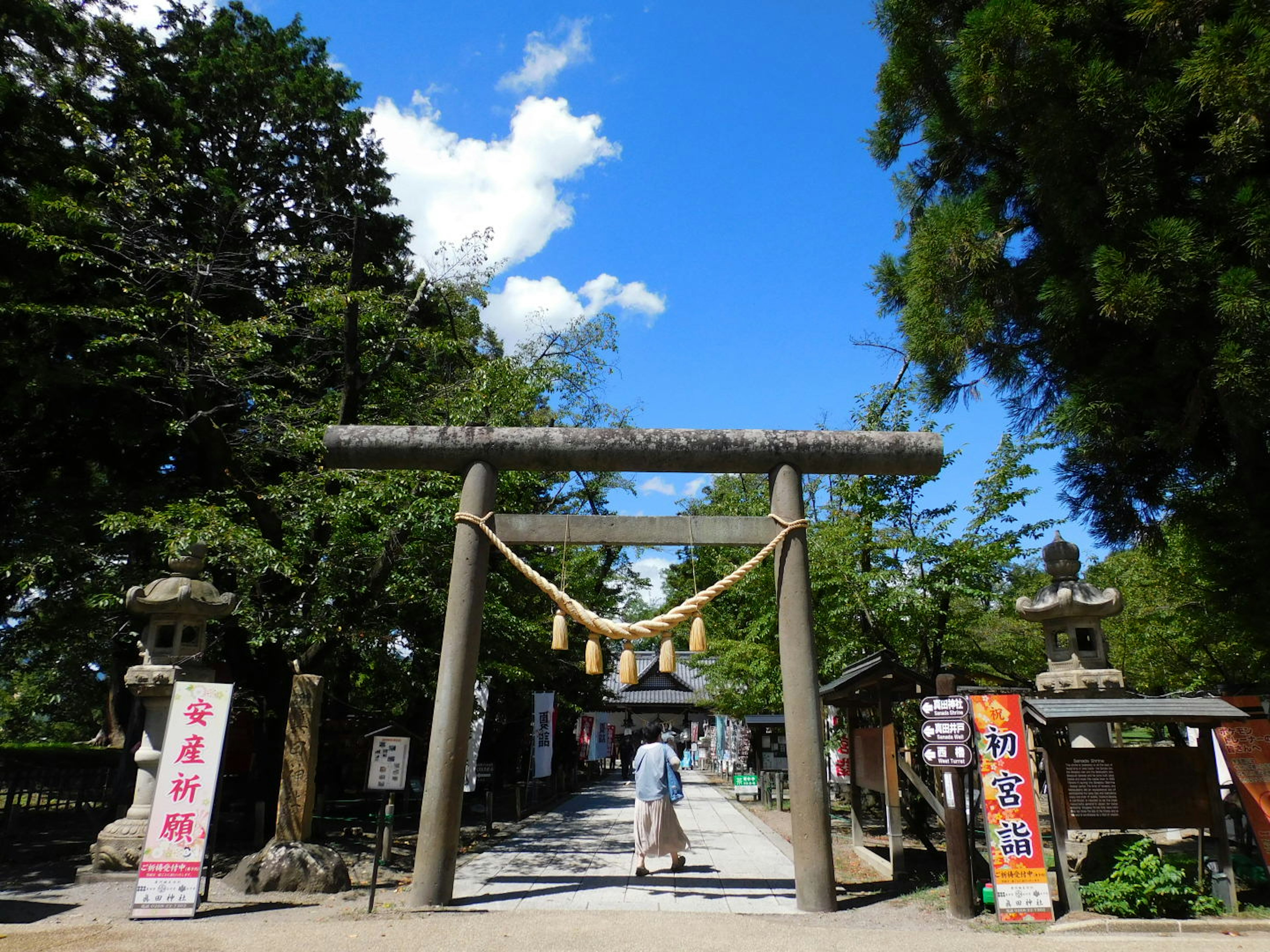 Una persona caminando a través de un torii en un santuario bajo un cielo azul