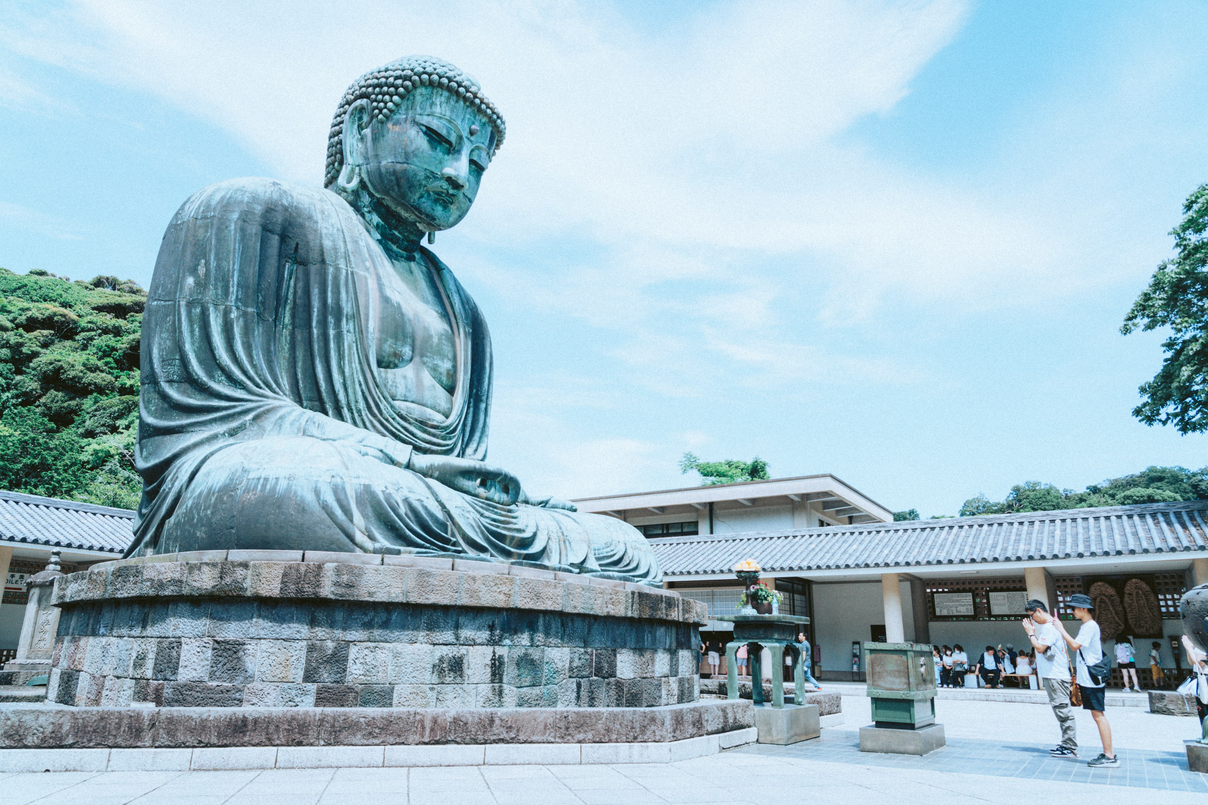 青空の下に座る大仏とその周りの観光客