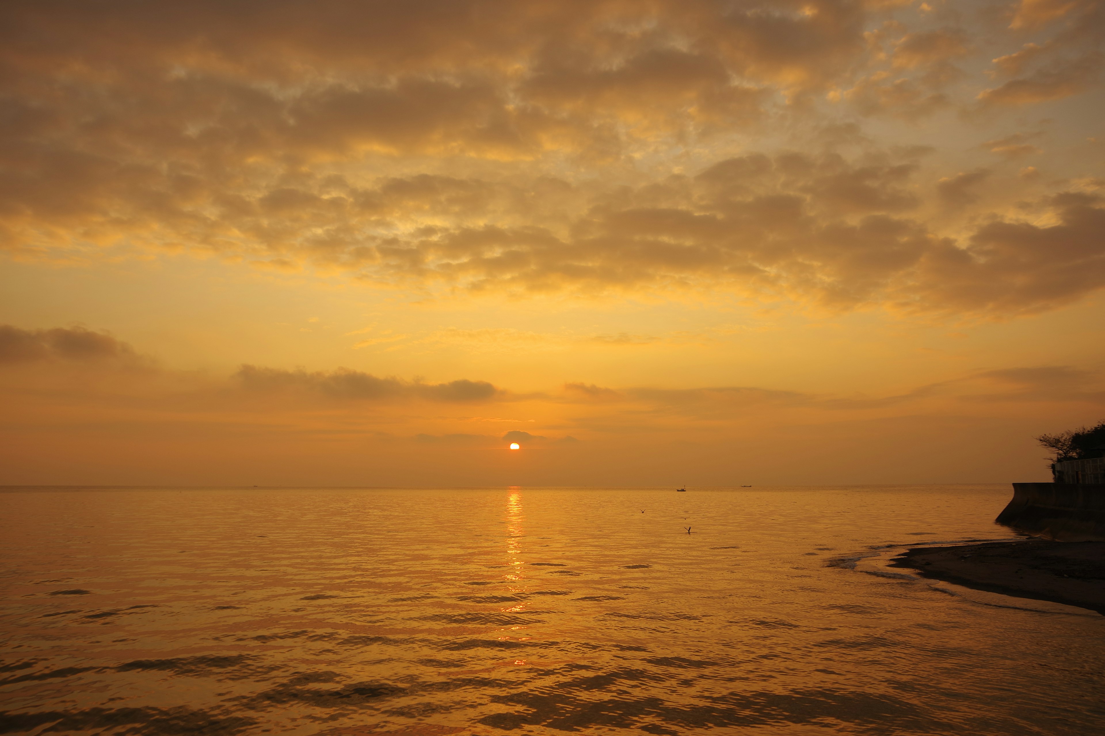 Atardecer sobre el mar tranquilo con nubes doradas y agua reflectante