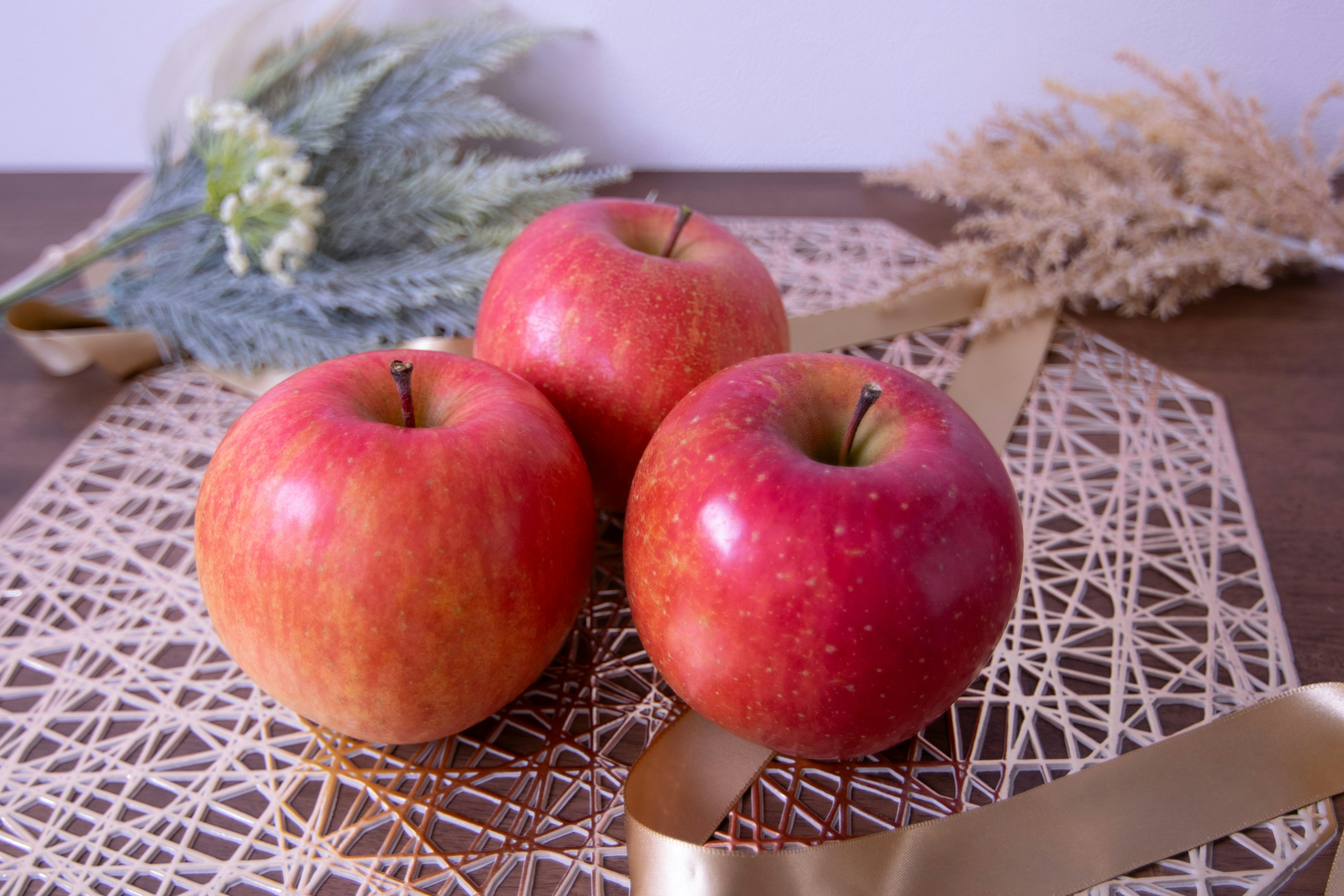 Trois pommes rouges disposées sur une surface décorative avec des fleurs séchées