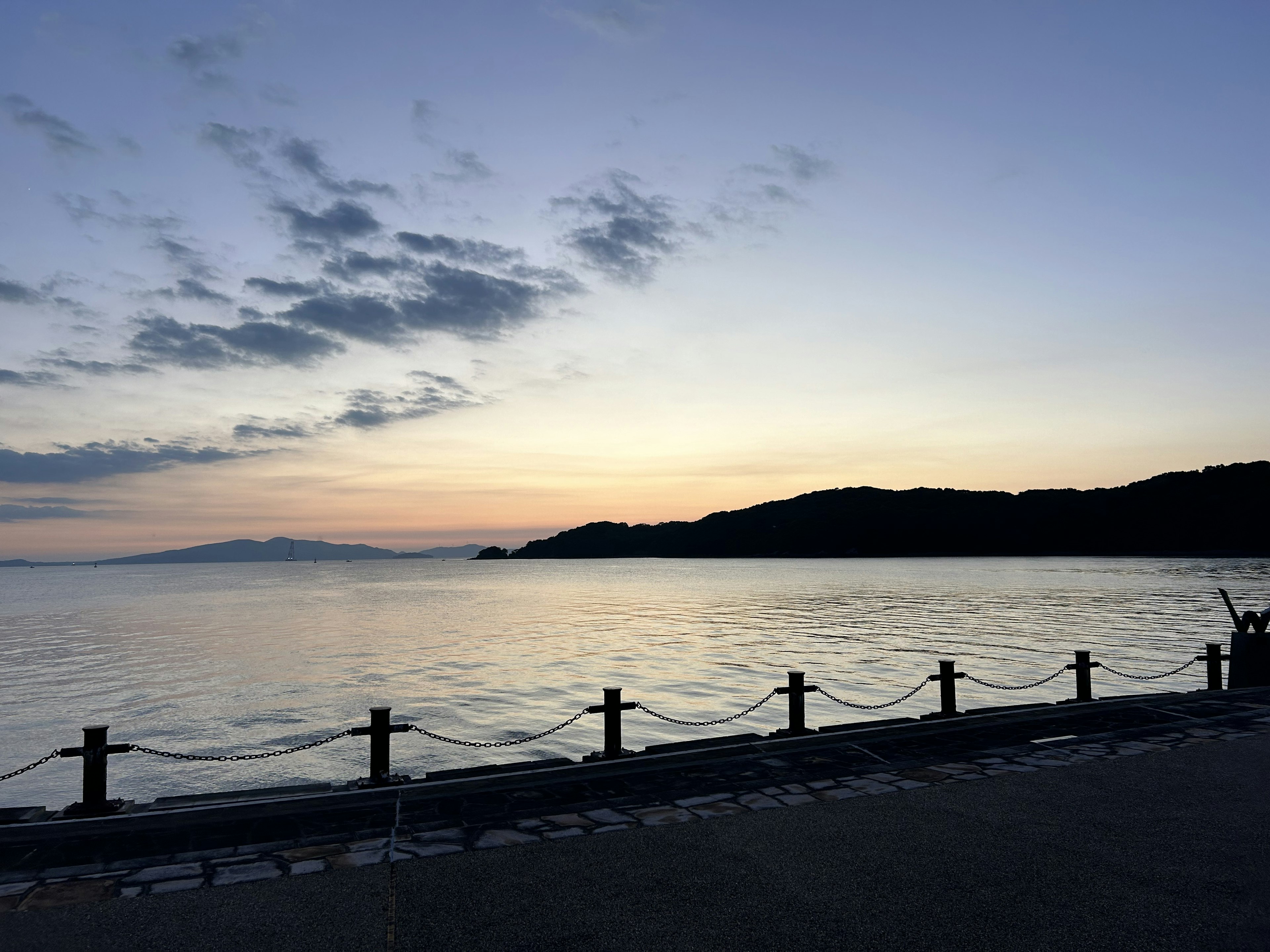 夕暮れの海岸線に沿った穏やかな水面と山々のシルエット