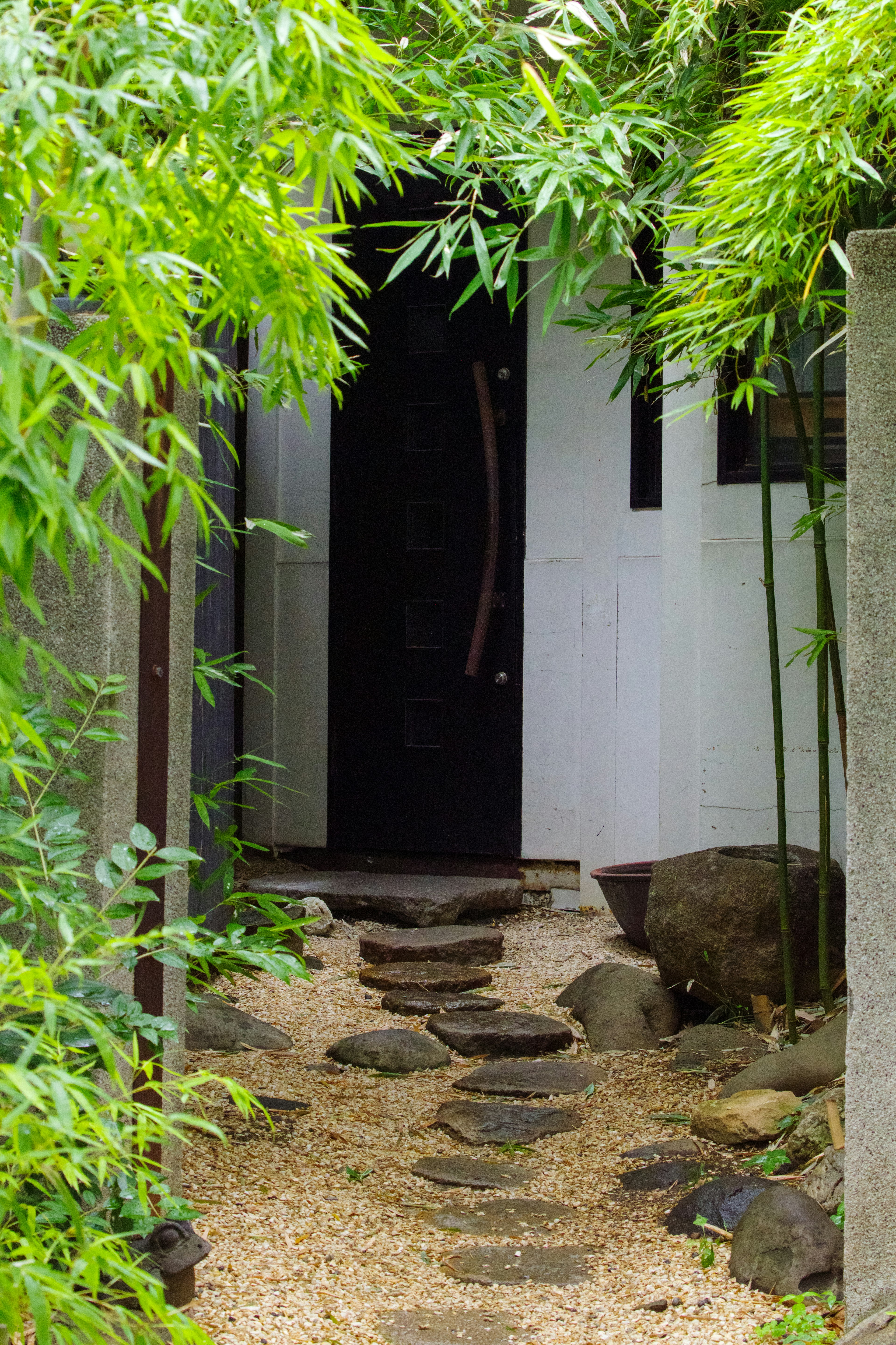 Jalan batu menuju pintu hitam dikelilingi oleh bambu hijau