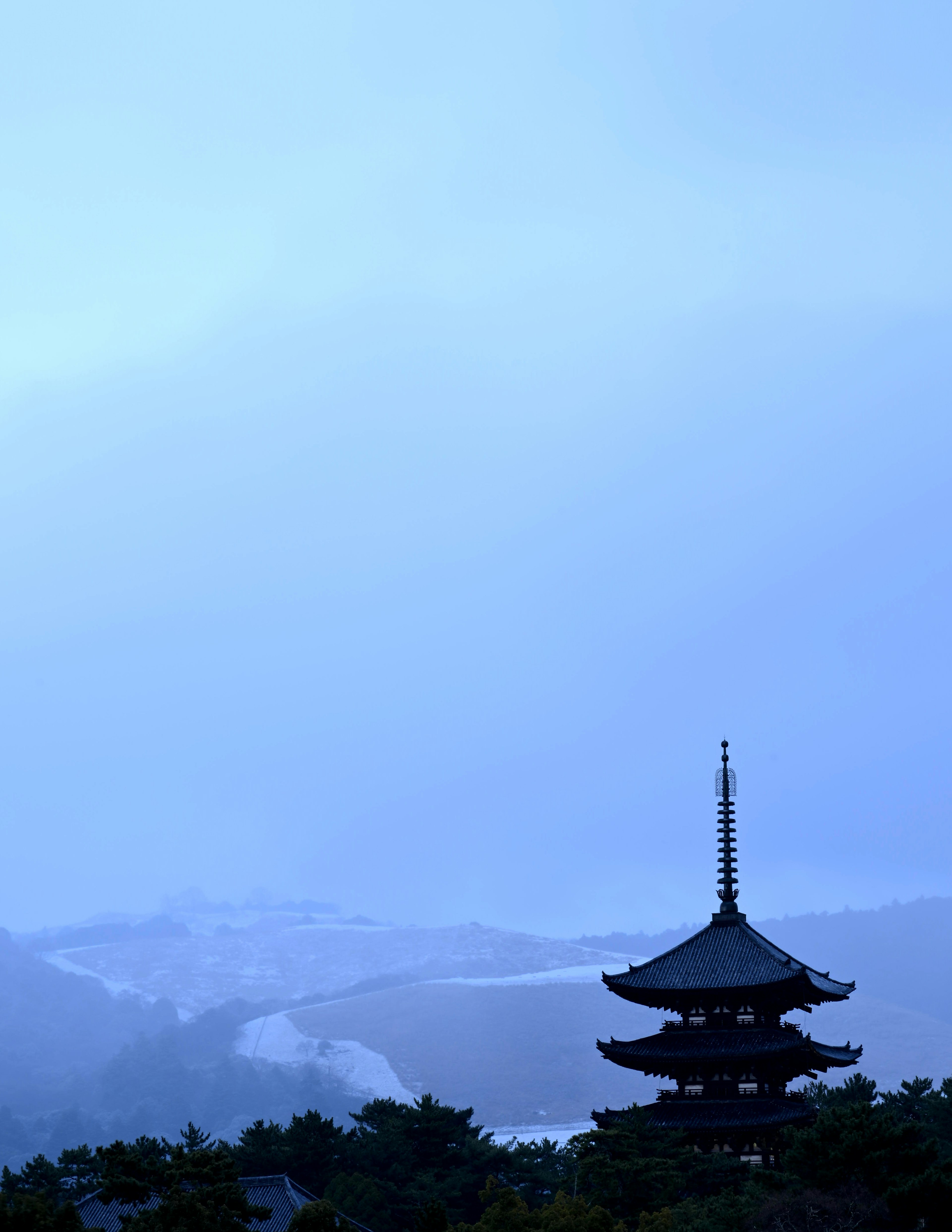 Silhouette of a pagoda against a blue sky with snow-covered hills in the background