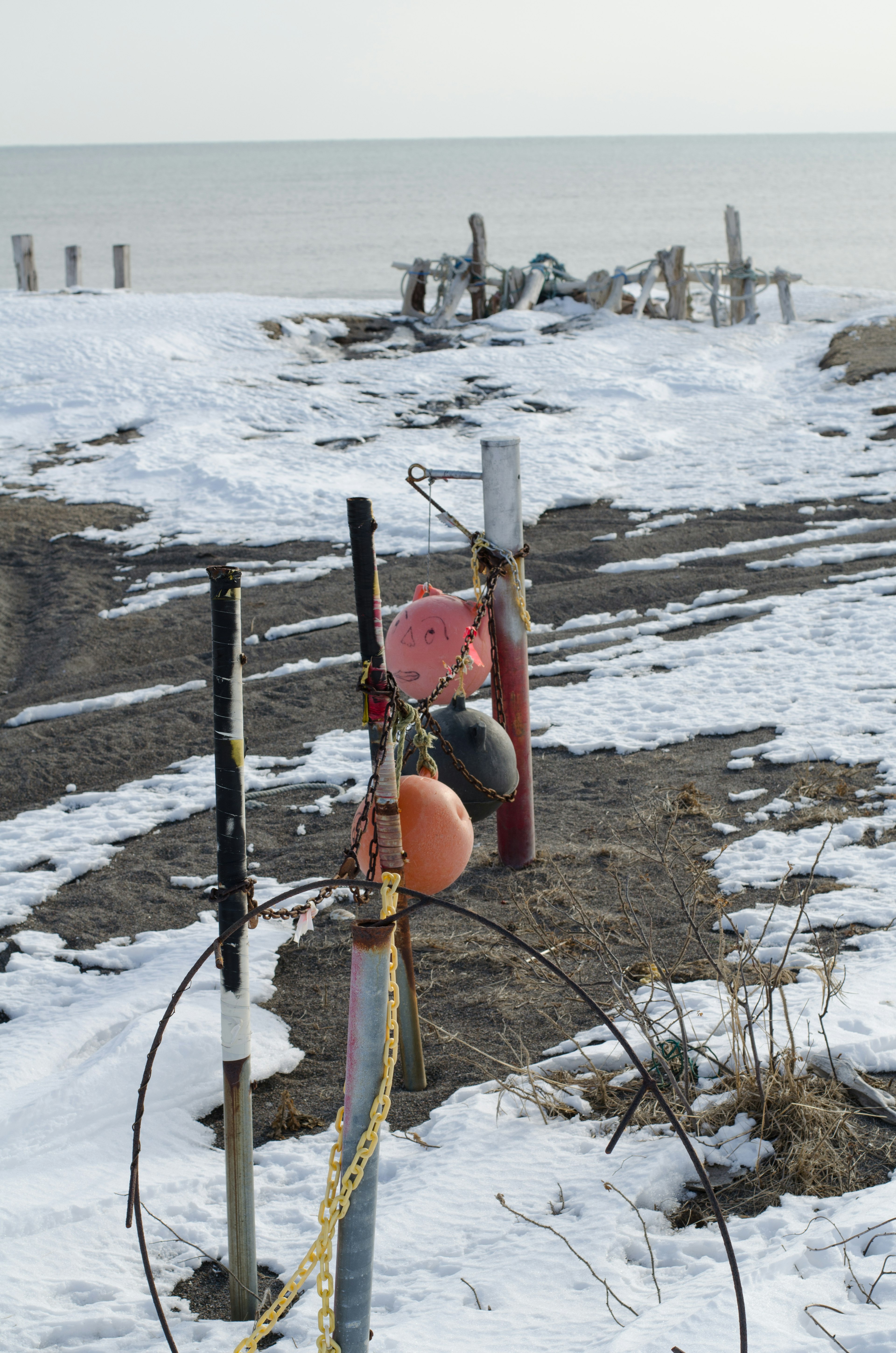 Eine Boje und Pfähle in einer verschneiten Strandlandschaft mit einem entfernten Ufer