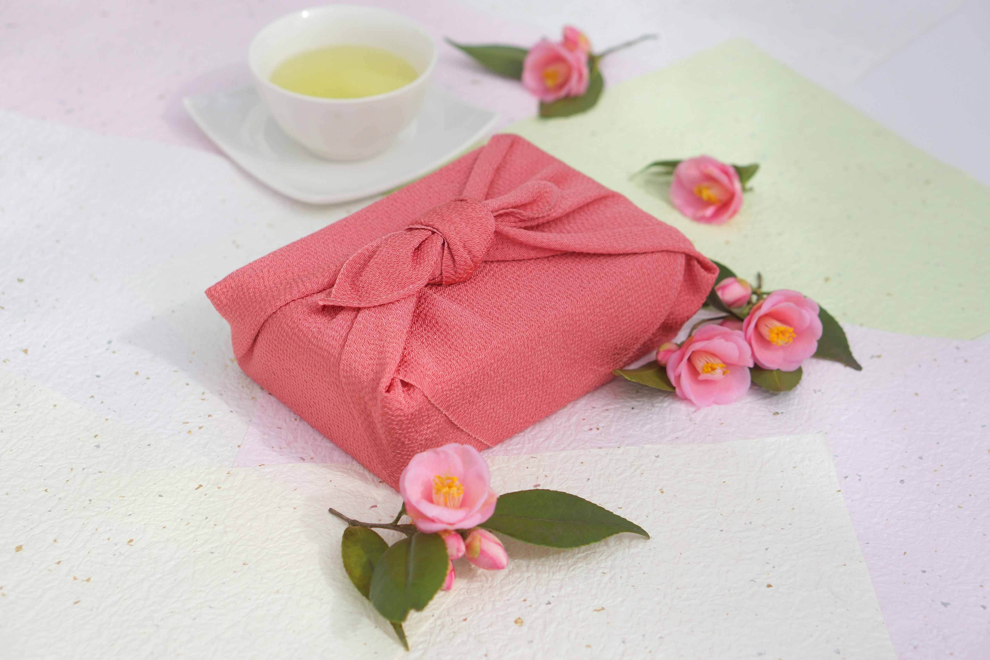 A pink wrapped gift with a cup of tea and decorative flowers around it