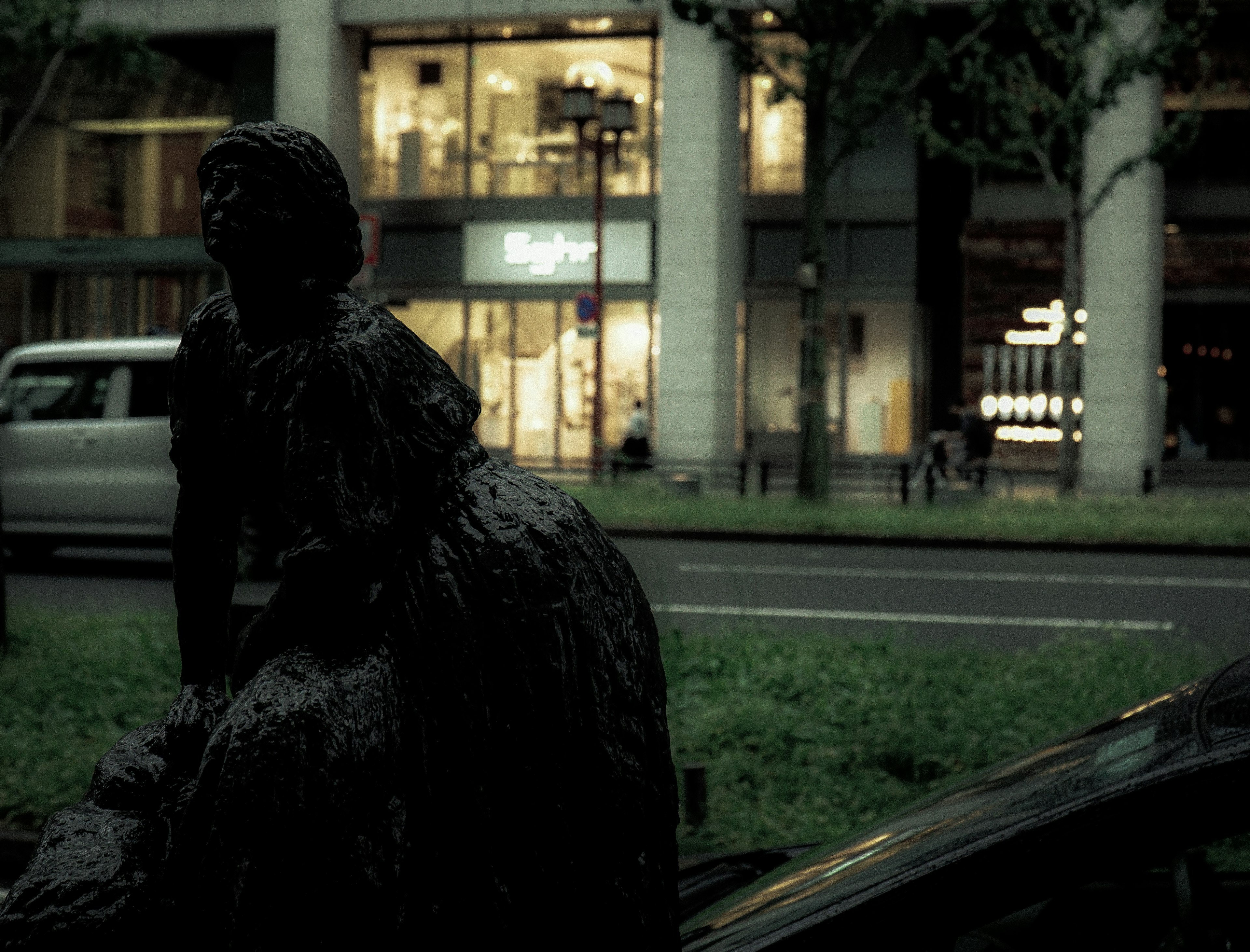 Black statue in an urban setting with store lights at night