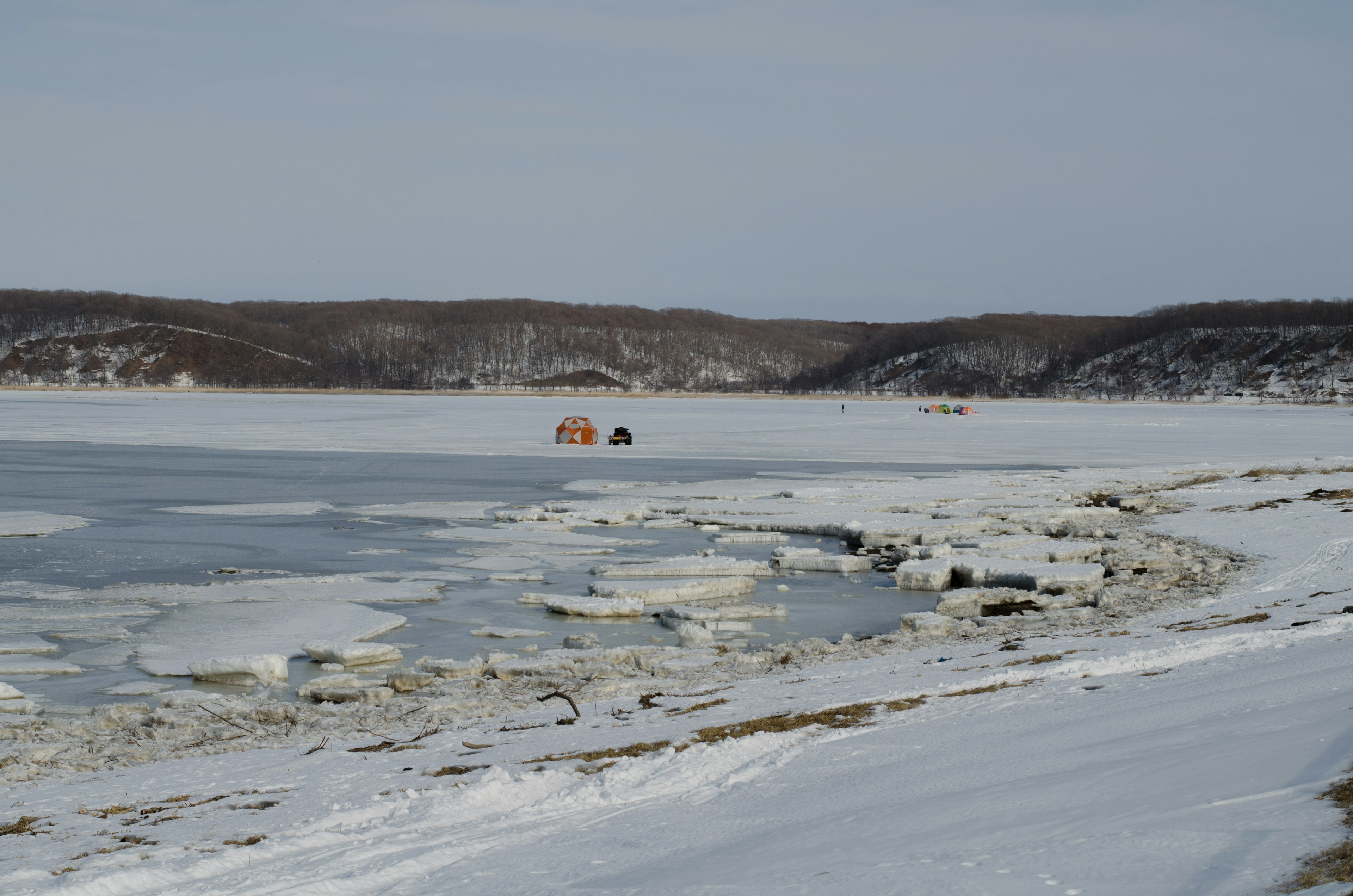 Lac gelé avec une rive enneigée et des cabanes rouges au loin