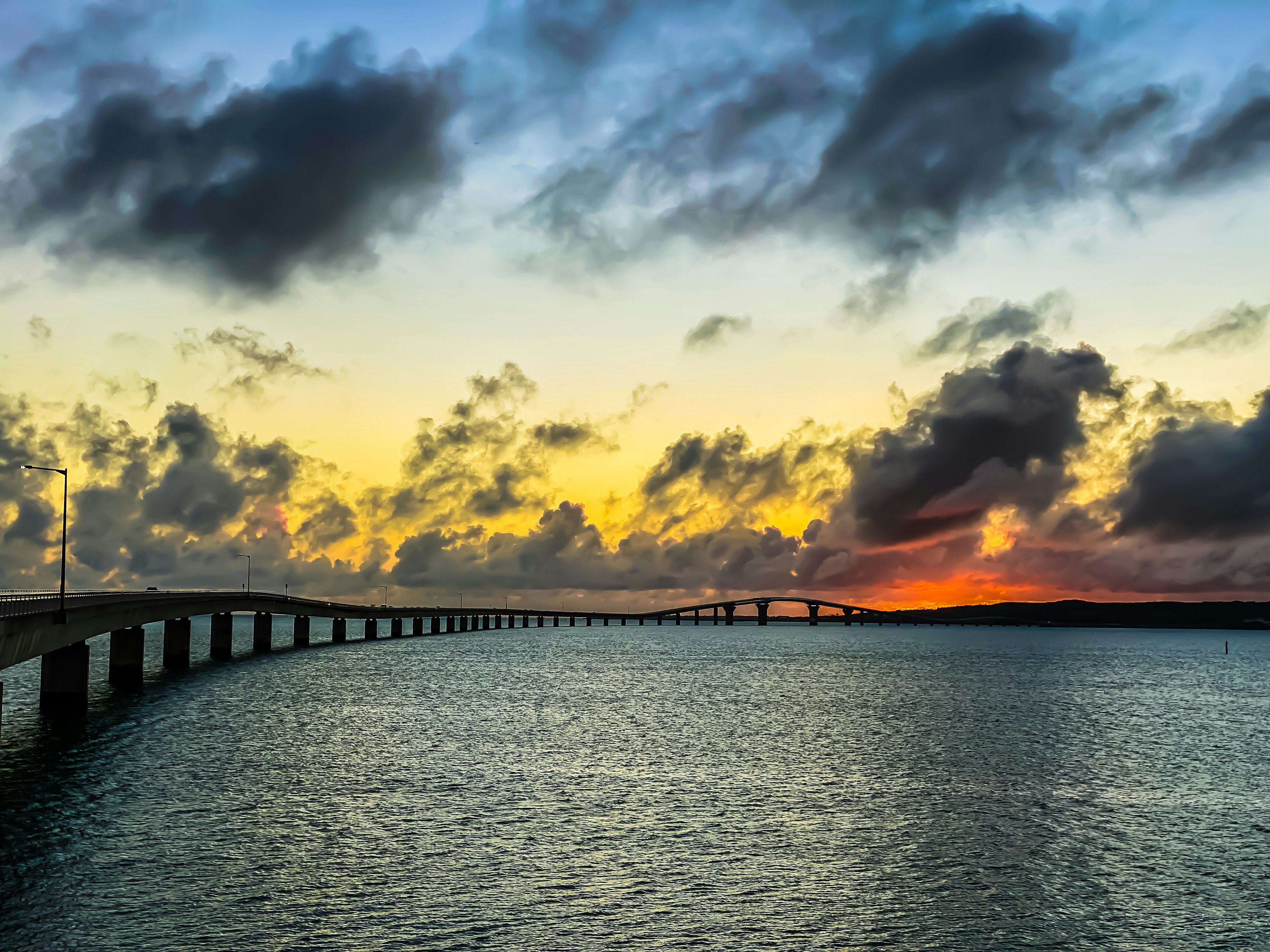 Largo puente sobre el mar al atardecer con nubes coloridas