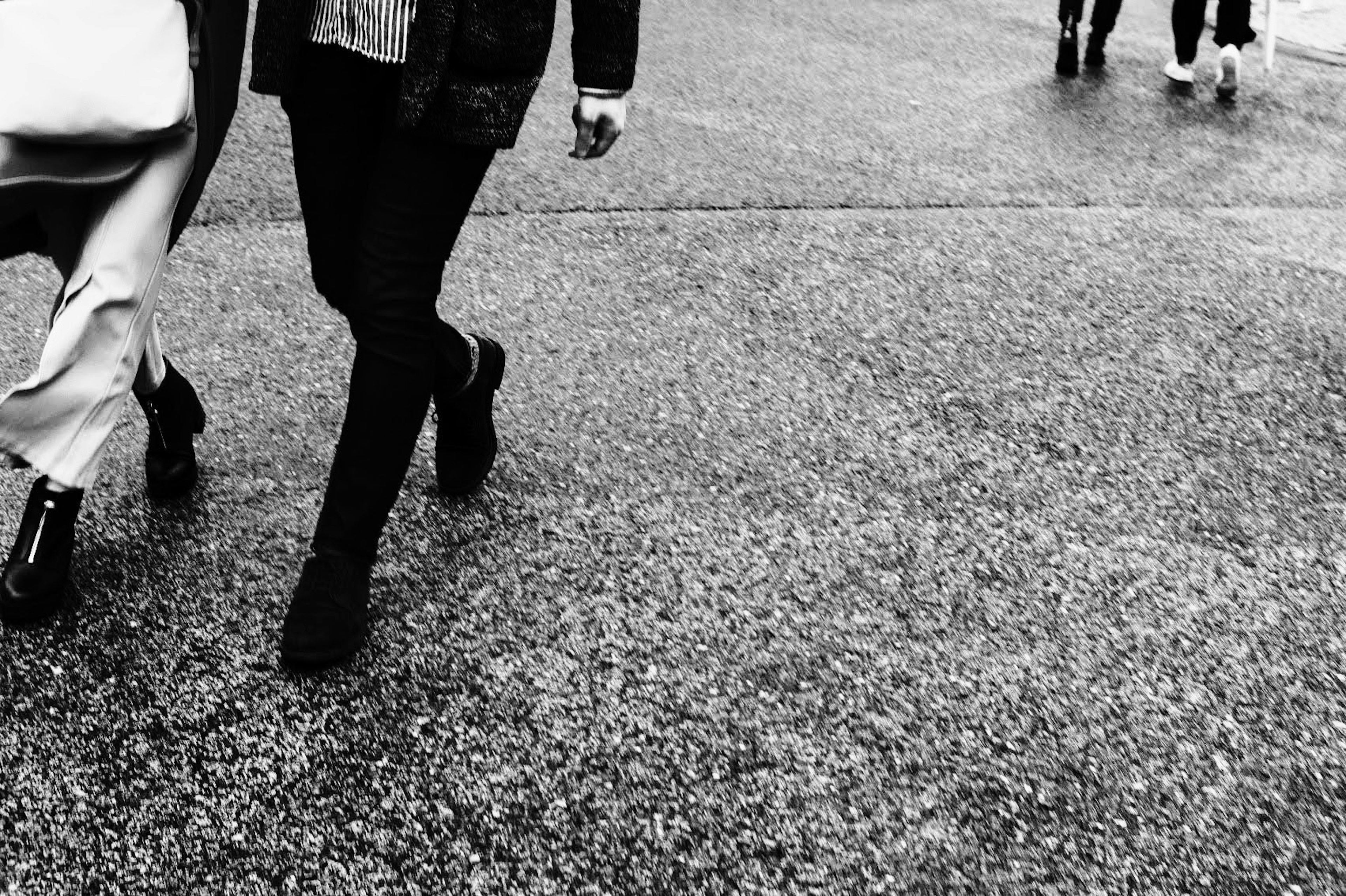 Black and white image of people's feet walking on a textured pavement