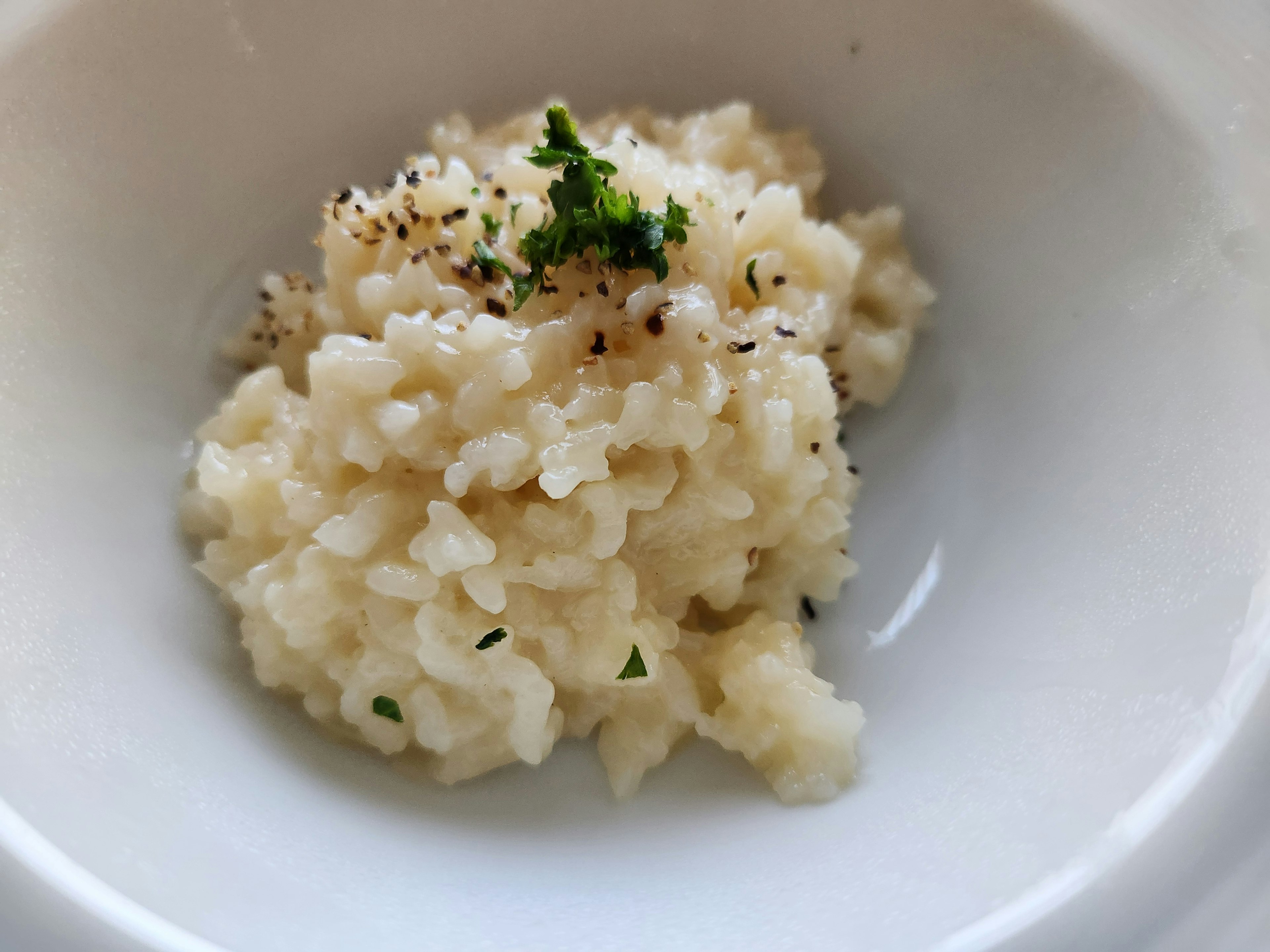 Risotto bianco cremoso guarnito con pepe nero e prezzemolo