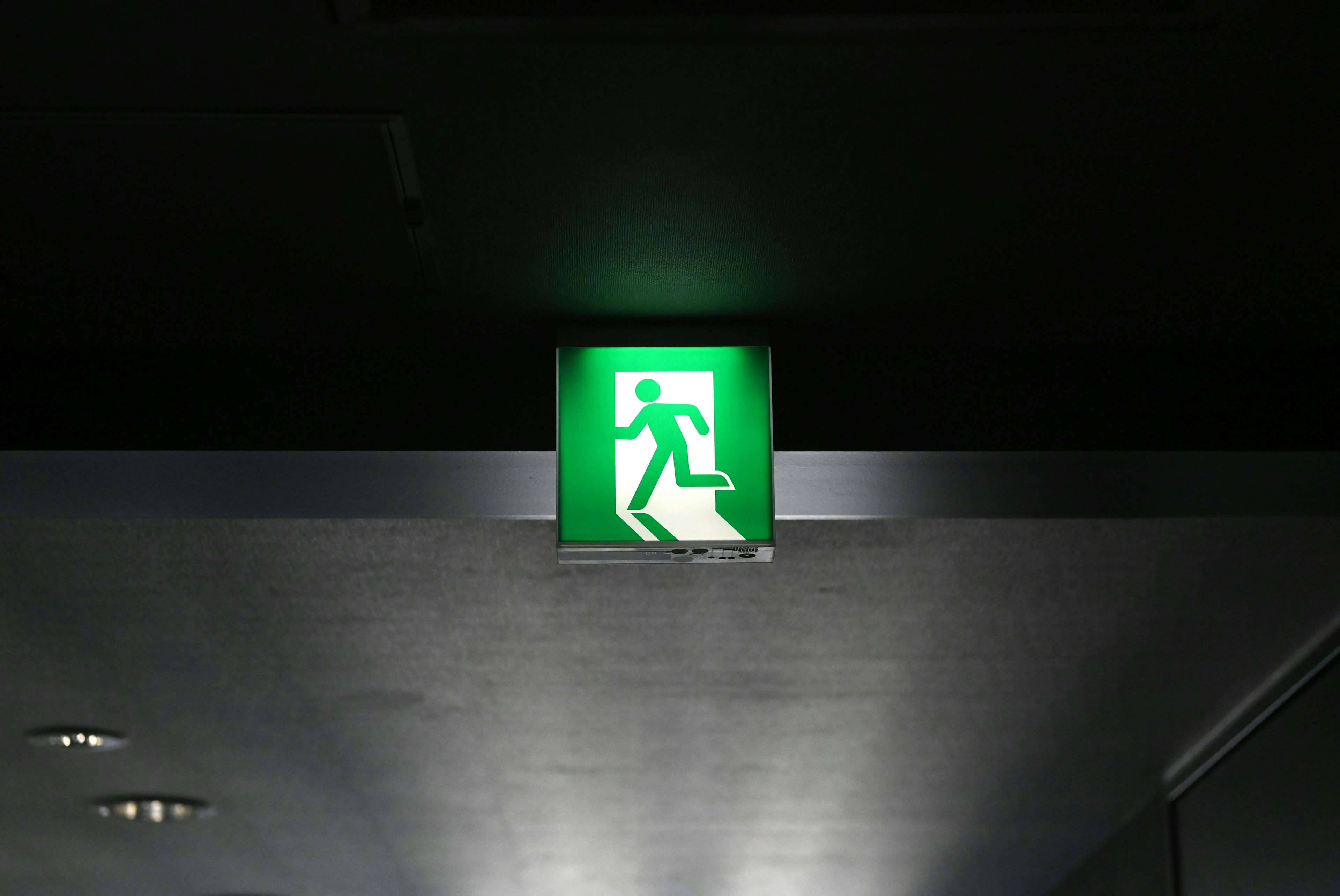 Illuminated green exit sign with a figure walking towards an exit on a dark background