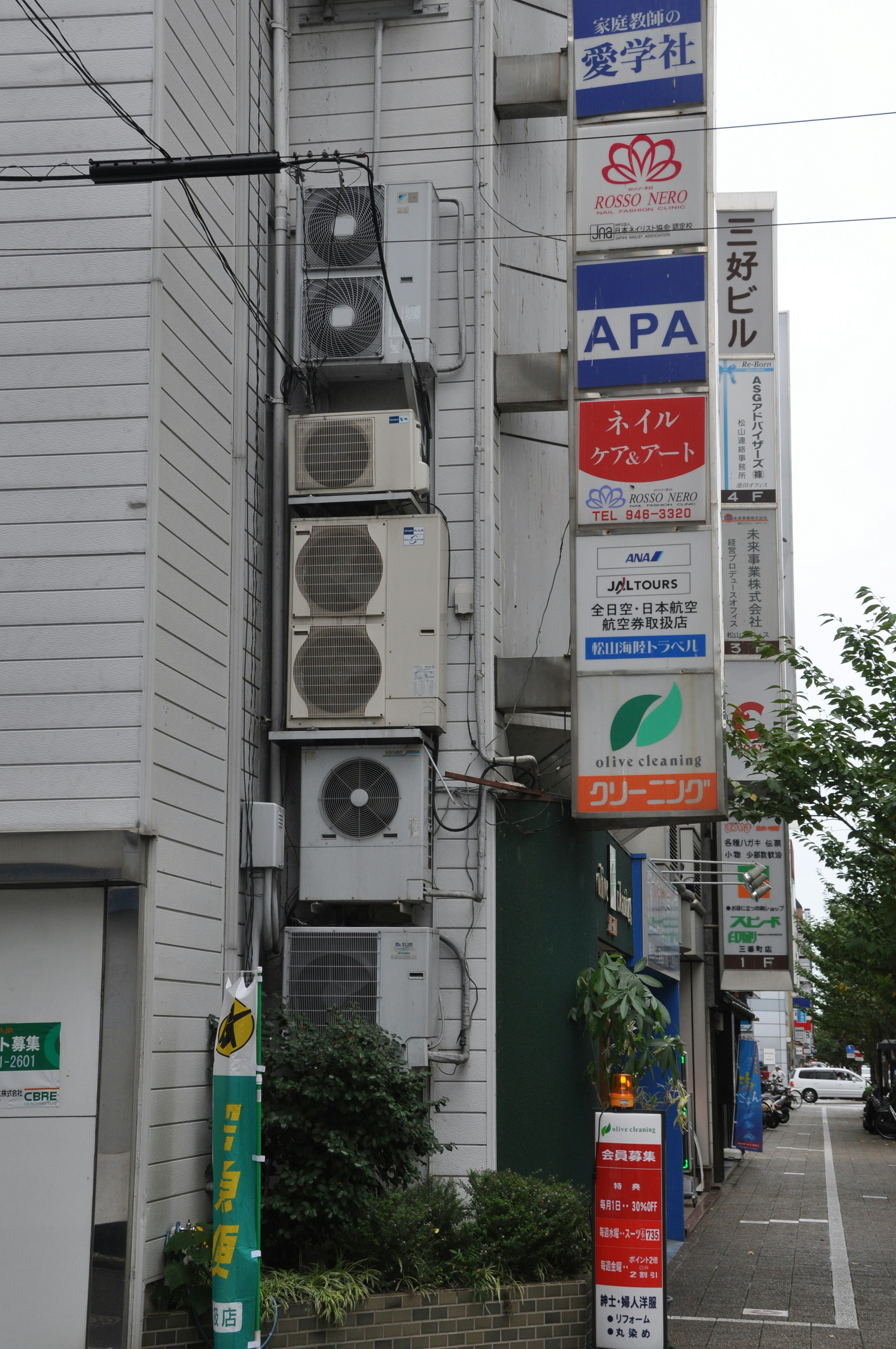 Lado de un edificio con múltiples unidades de aire acondicionado y varios letreros