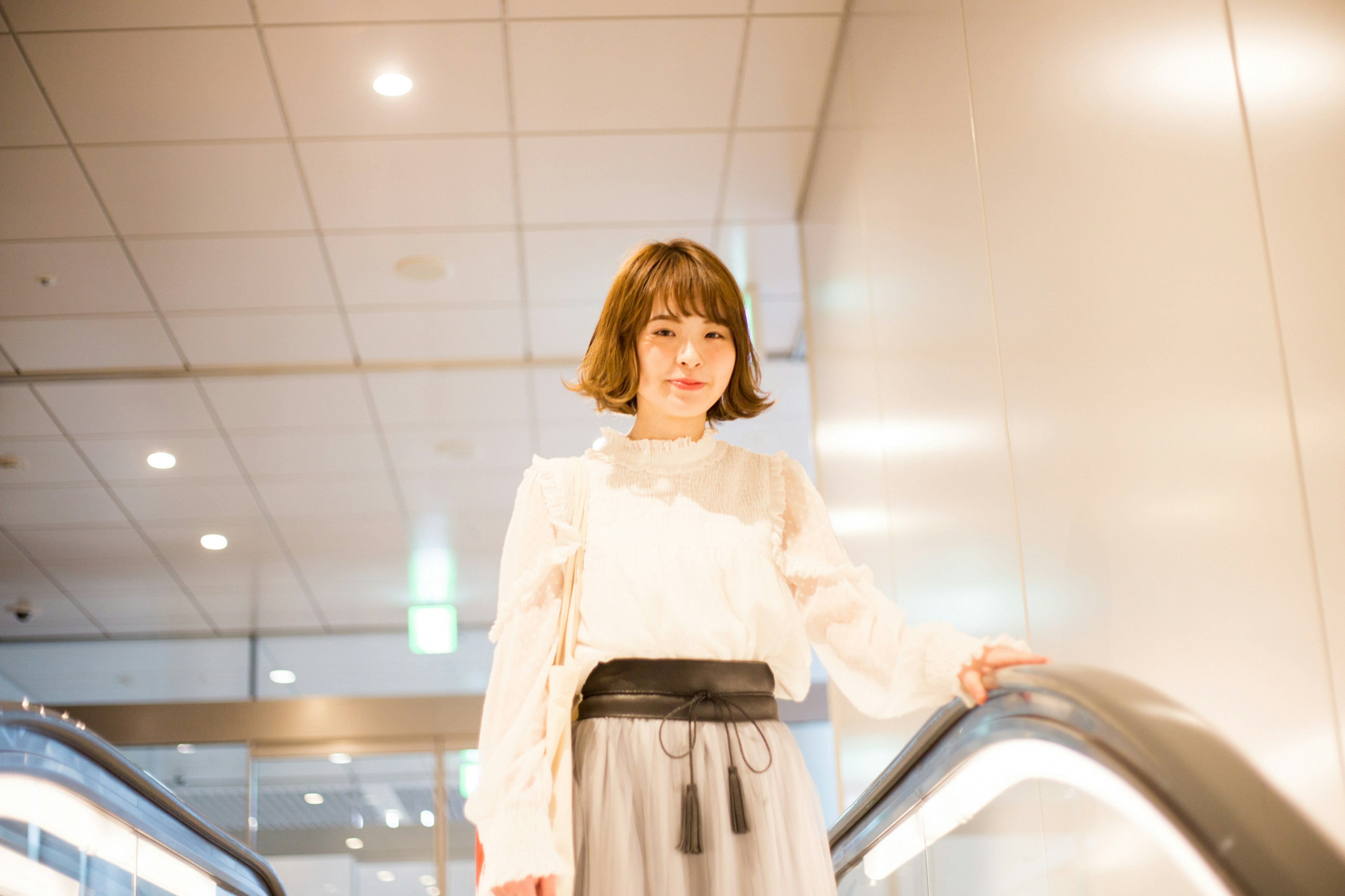 Fashion image of a woman standing on an escalator wearing a white blouse and gray skirt