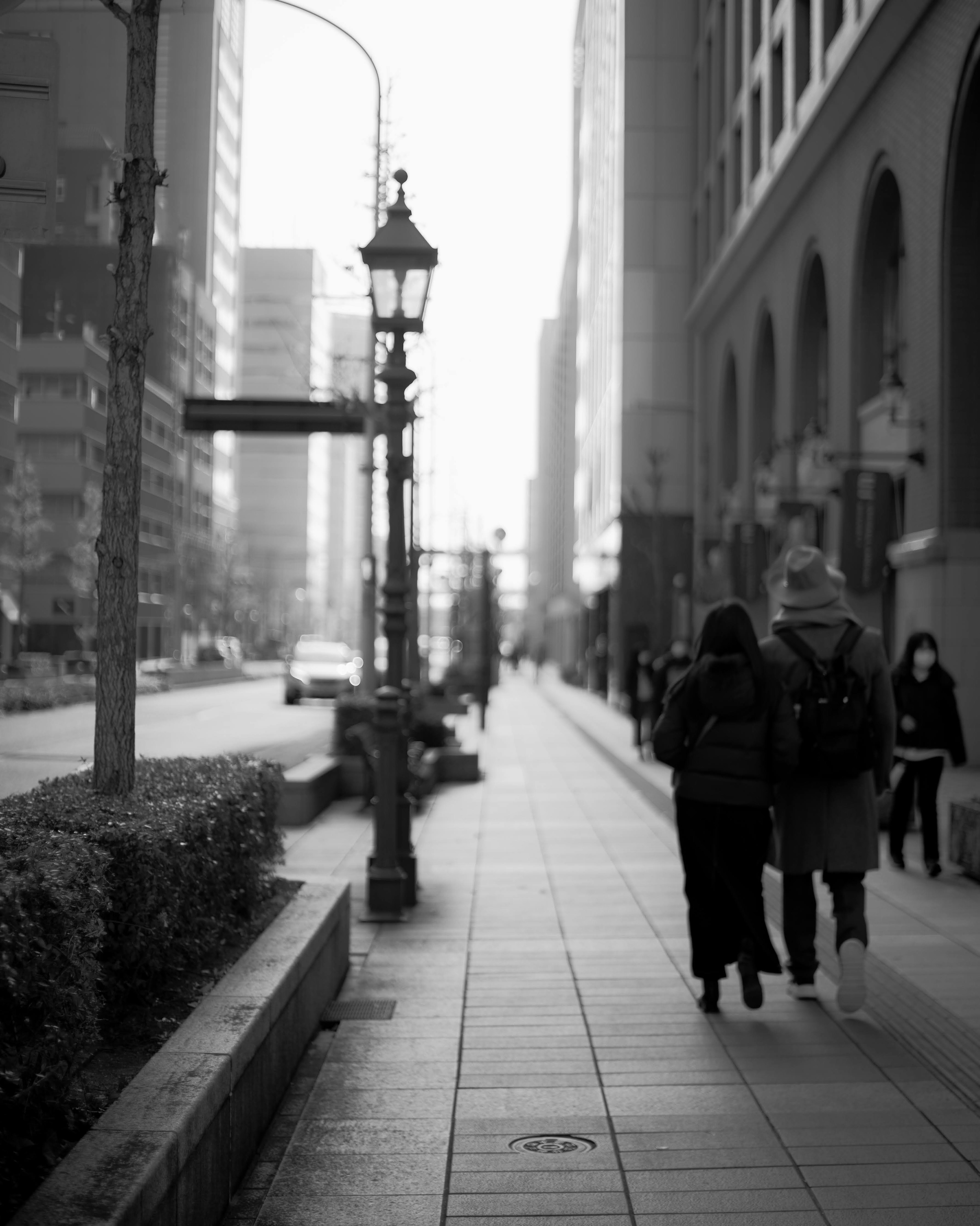 モノクロの都市景観で歩道を歩く二人の人物と街灯