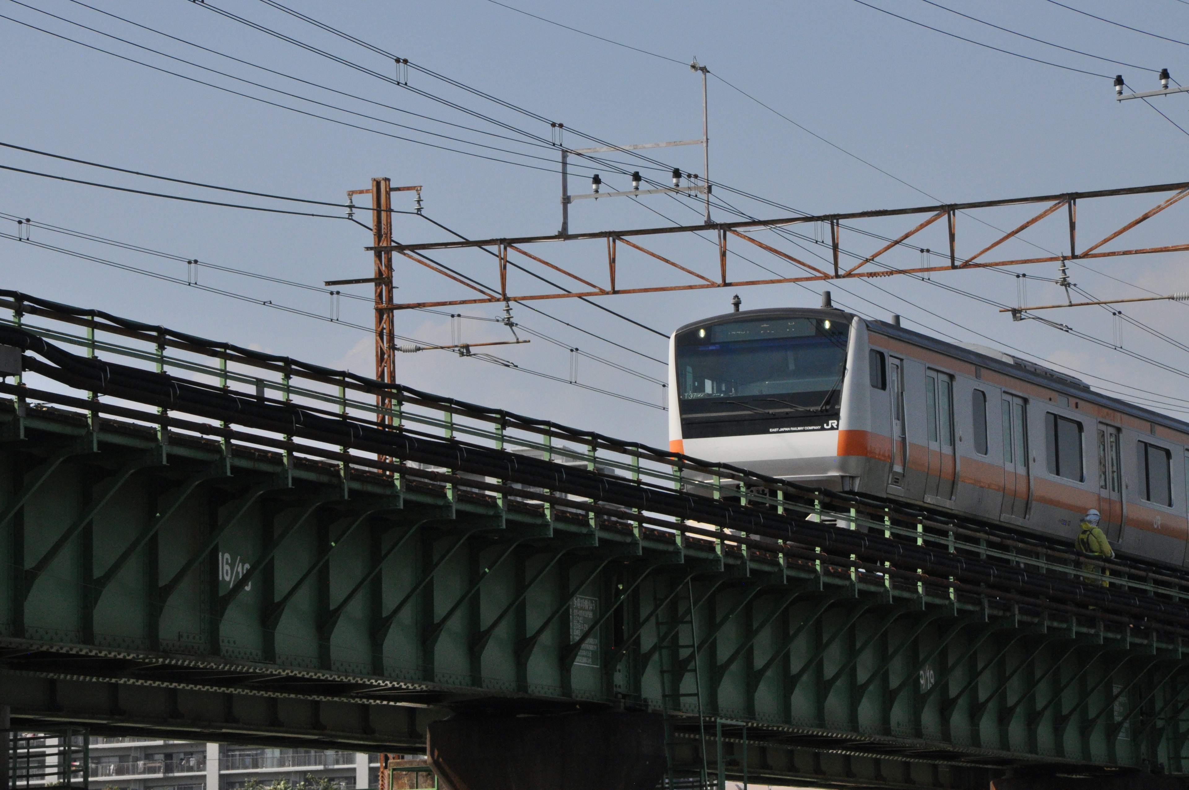 รถไฟฟ้าสายชานเมืองวิ่งอยู่บนสะพานรถไฟที่มีพื้นหลังเป็นท้องฟ้าสีฟ้า