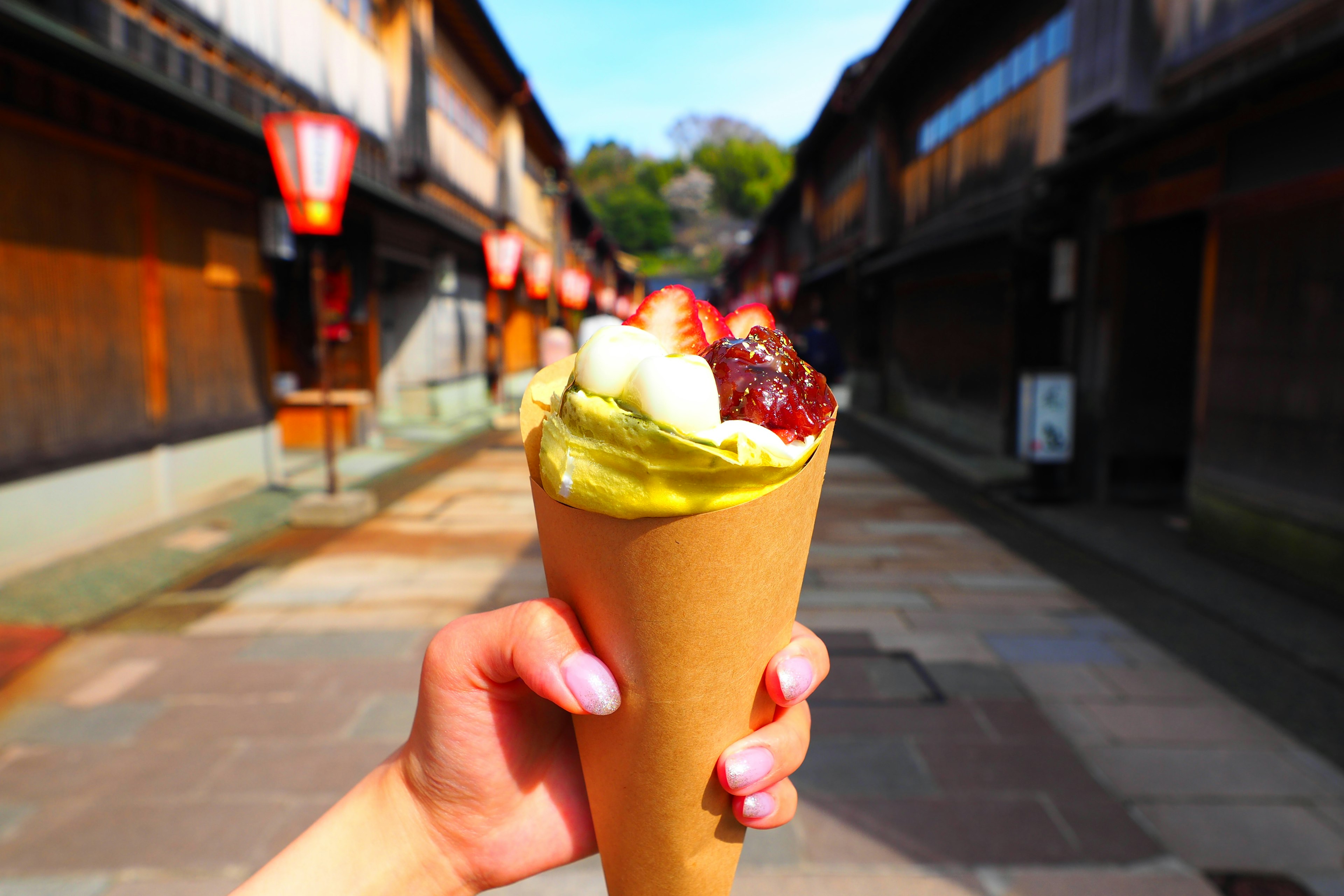 Mano sosteniendo un cono de helado de matcha con una calle tradicional de fondo