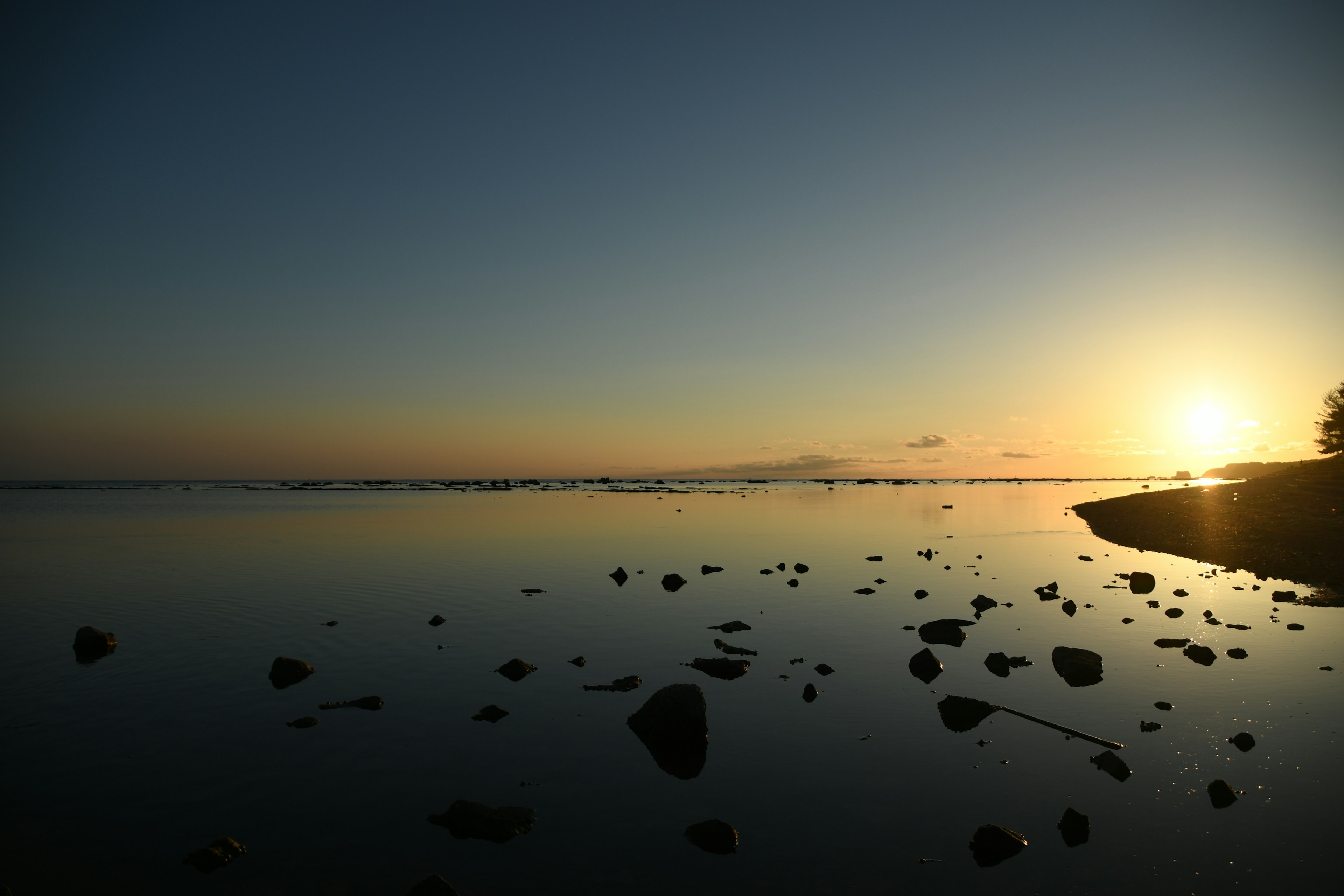 静かな海の景色と夕日の反射岩のある海岸