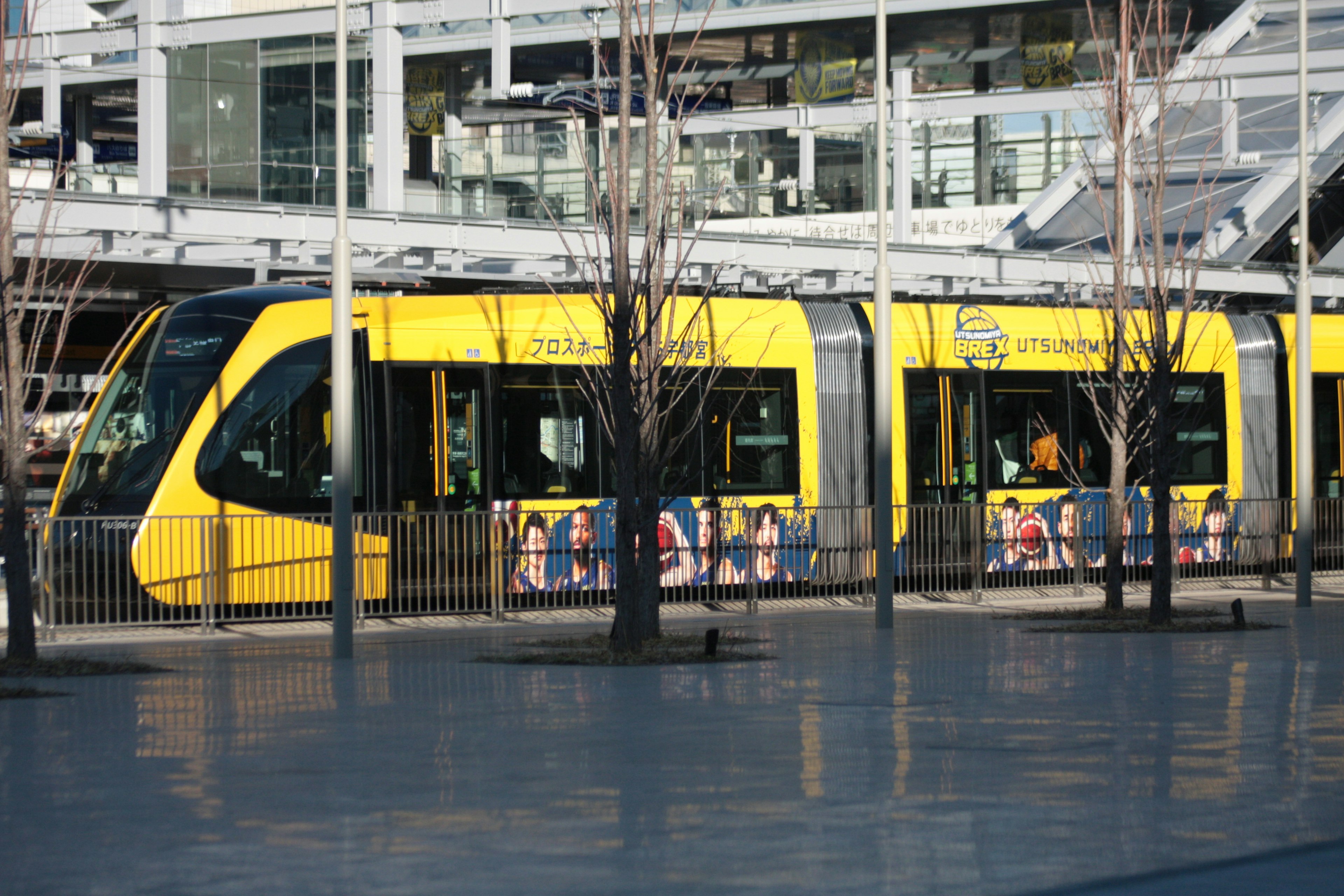 Eine gelbe Straßenbahn, die an einer Haltestelle mit Werbung an der Seite hält