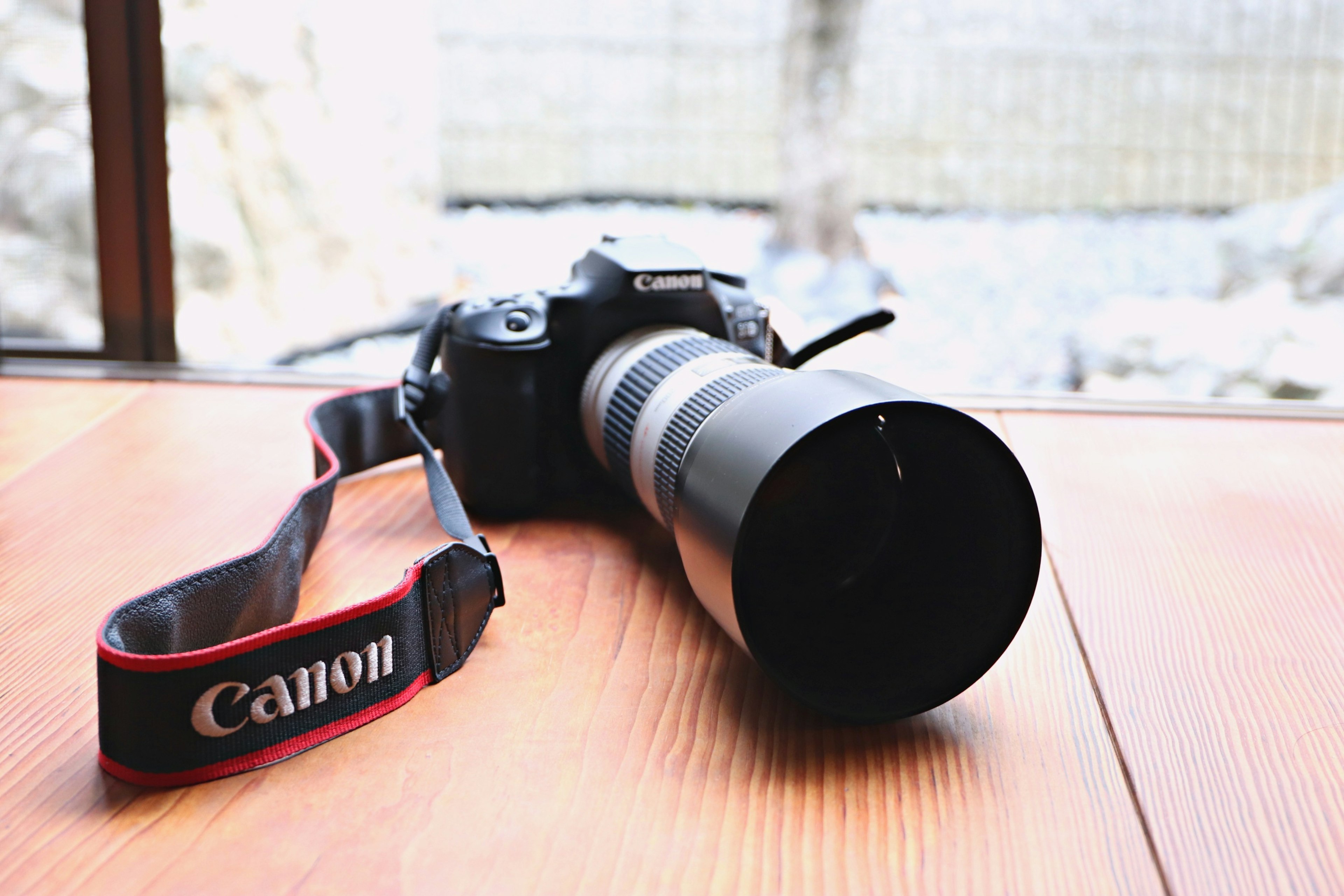 Un appareil photo Canon avec un grand objectif posé sur une table en bois