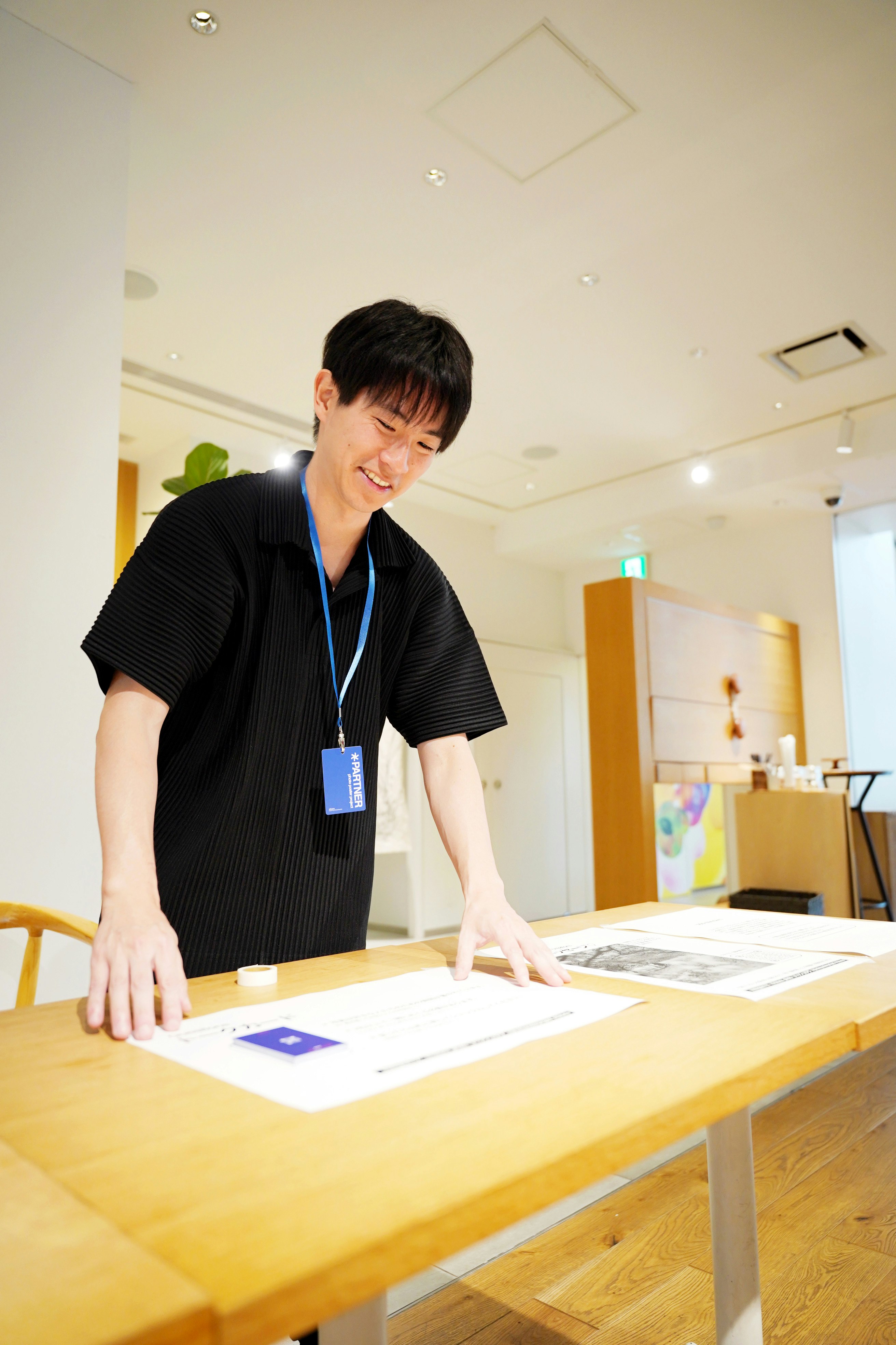 Một người đàn ông mỉm cười đứng bên bàn trưng bày tác phẩm nghệ thuật trong không gian trong nhà