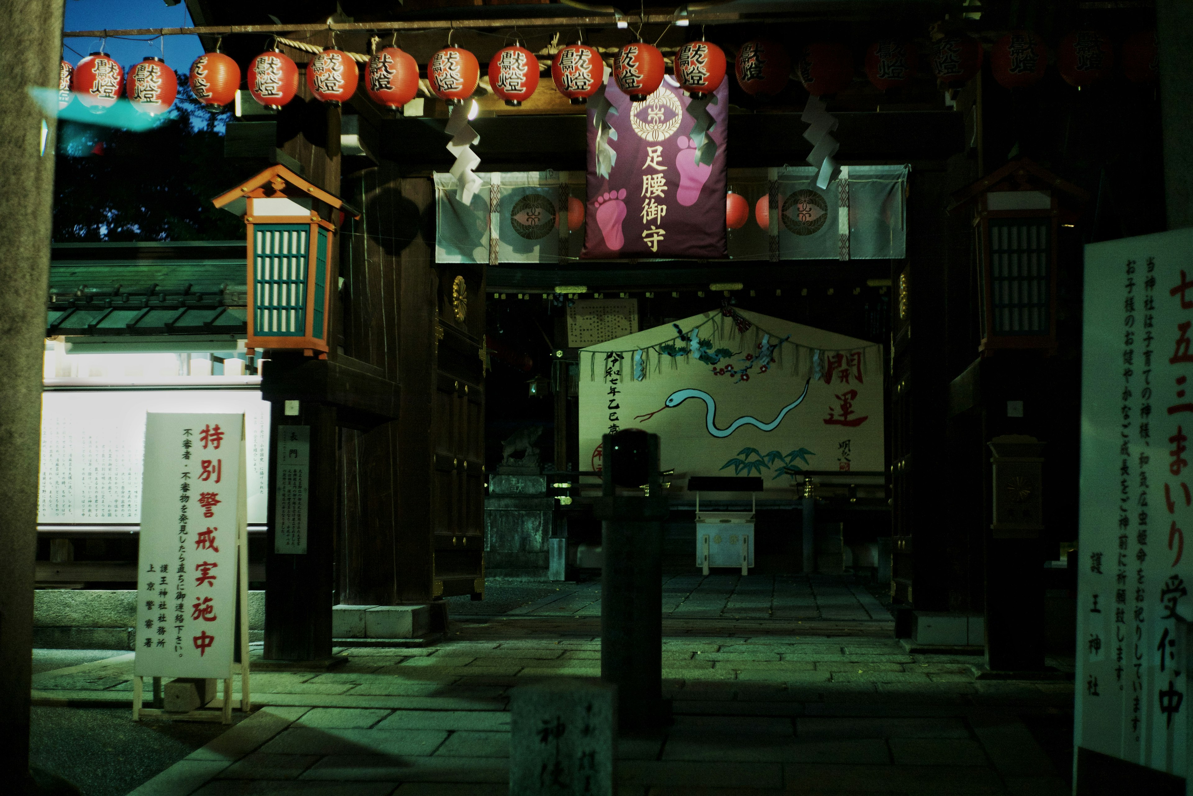 Entrance of a shrine at night with lanterns and signs