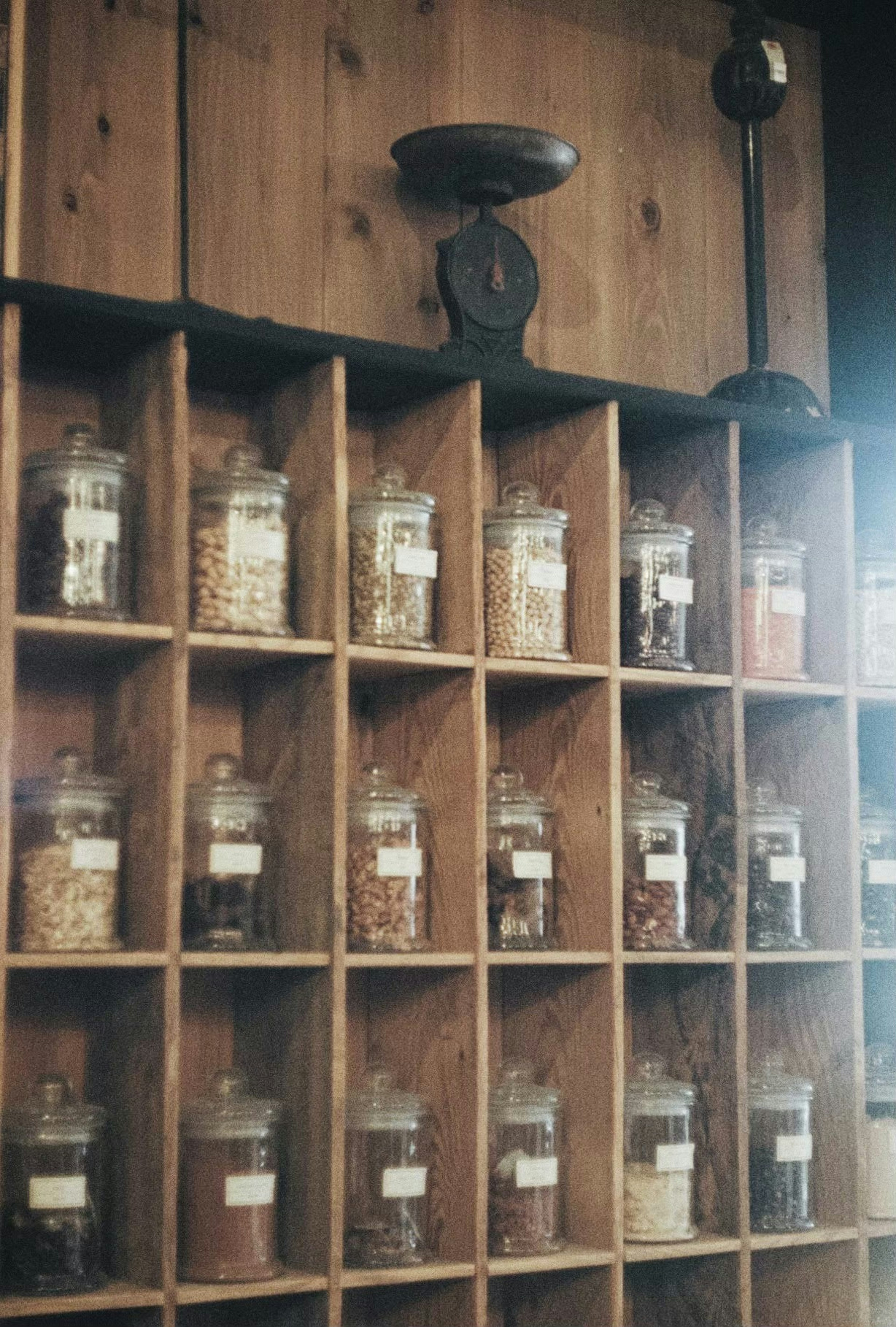 Glass jars filled with various contents arranged on a wooden shelf with labels and an old scale mounted above