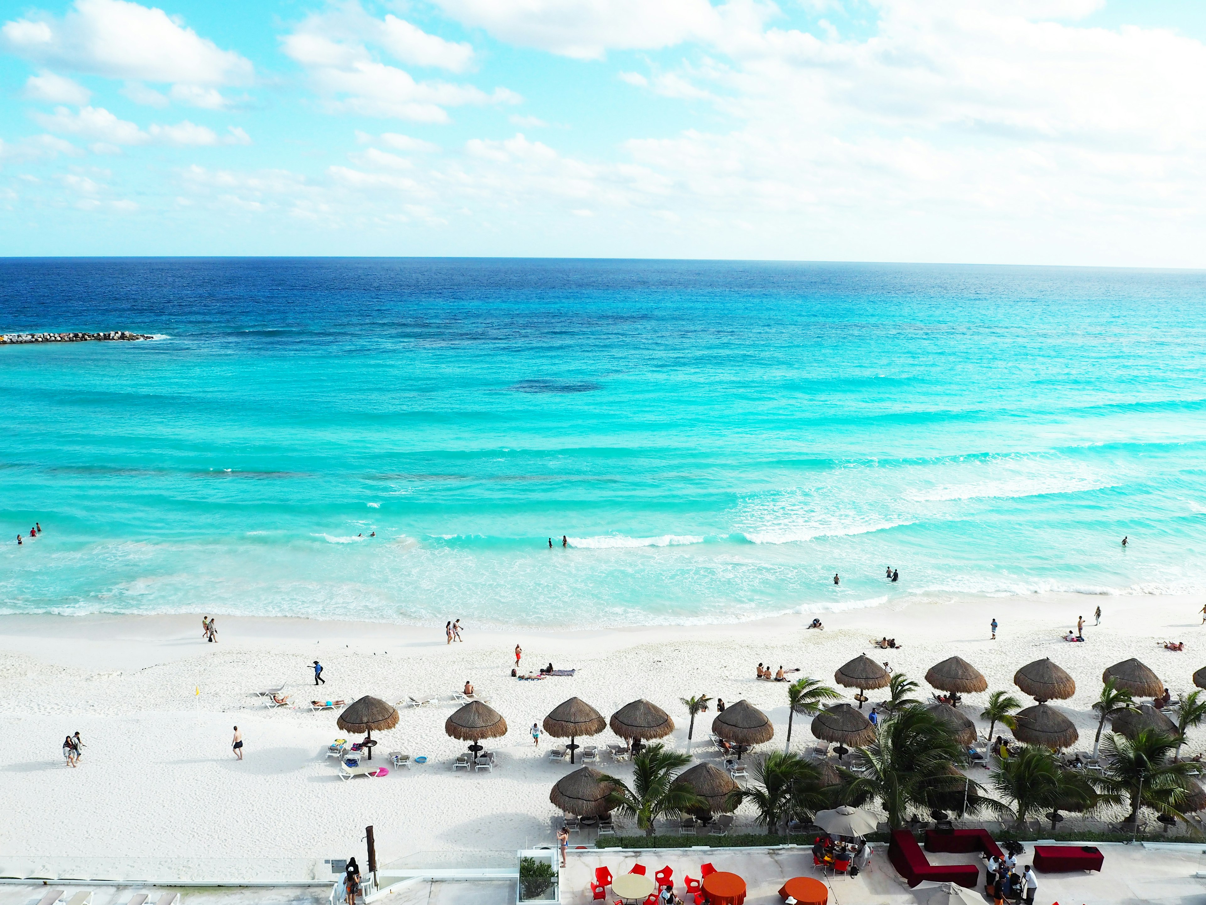 View of a beach with blue ocean and white sand umbrellas and people visible