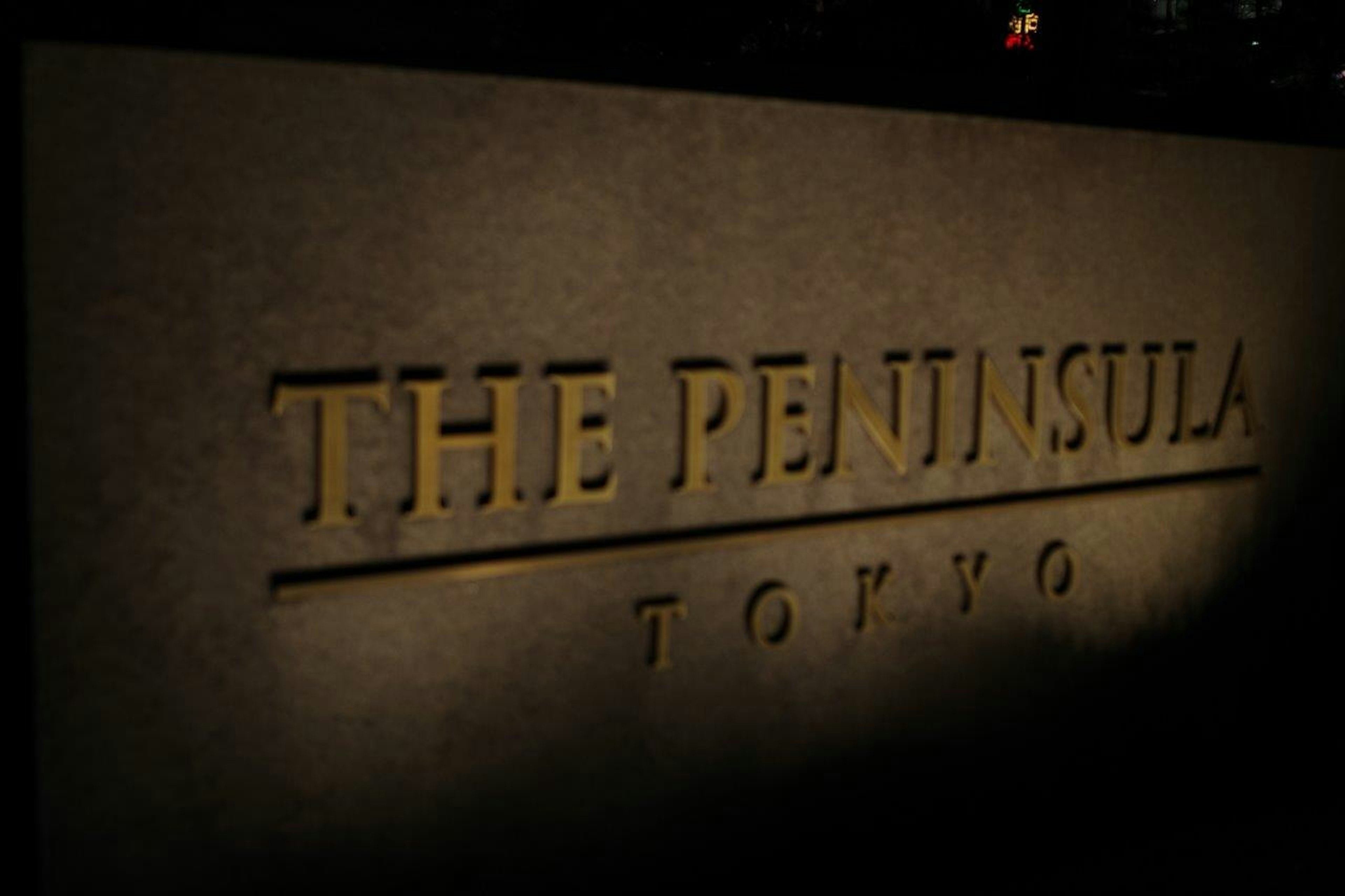 Schild des Peninsula Tokyo bei Nacht beleuchtet mit goldenen Buchstaben