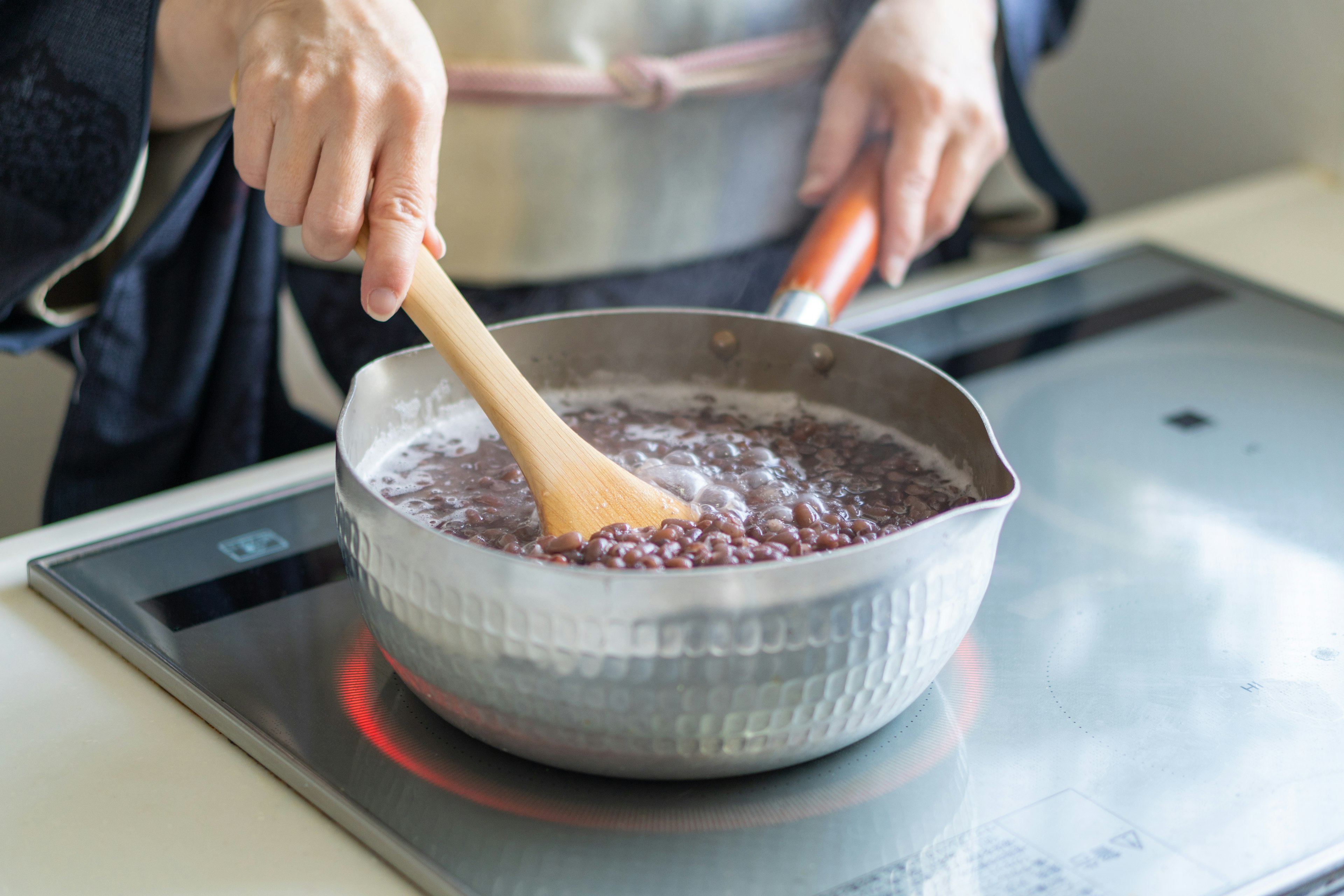 Gros plan des mains en train de remuer des haricots rouges dans une casserole sur une cuisinière