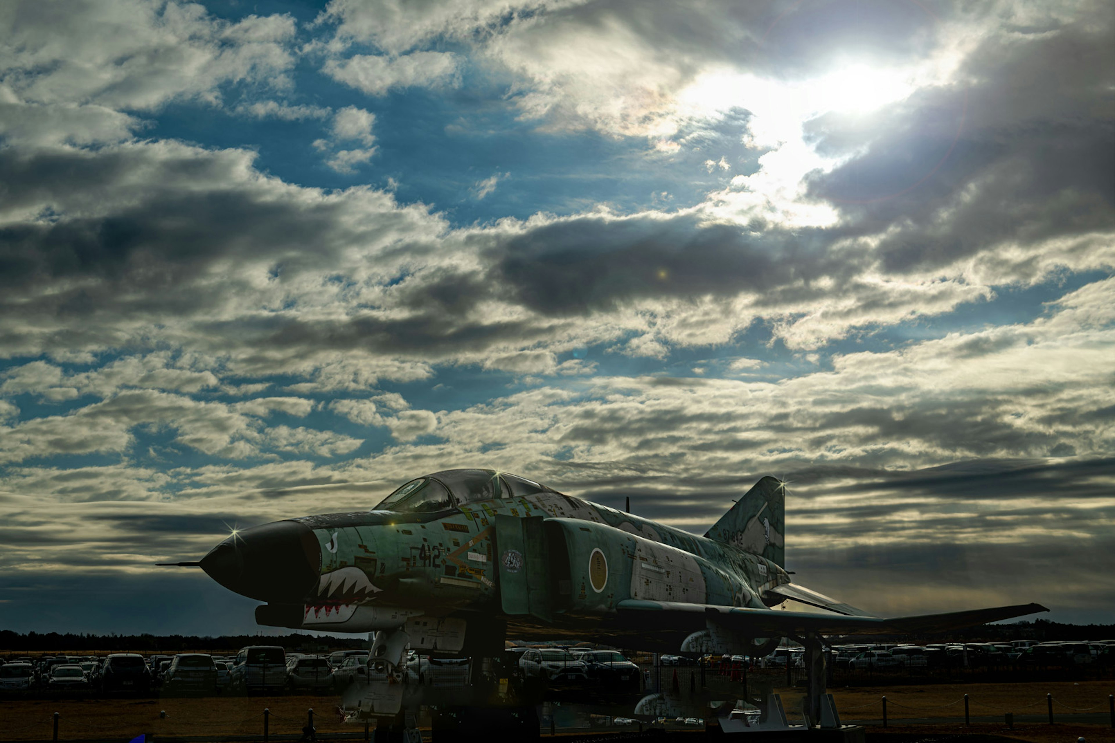 A fighter jet under a blue sky with clouds and sunlight shining