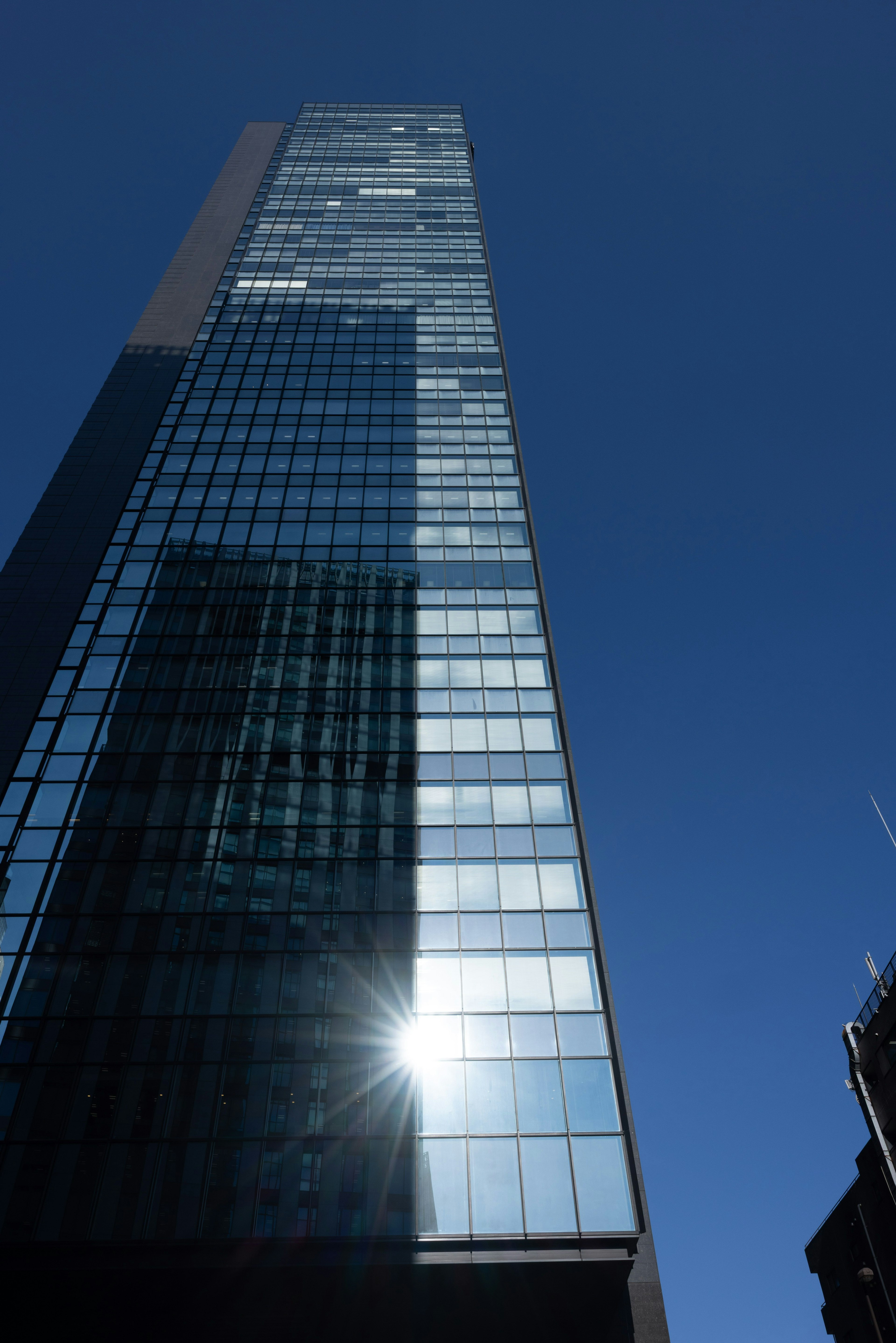 Hoher Wolkenkratzer, der Sonnenlicht gegen einen klaren blauen Himmel reflektiert