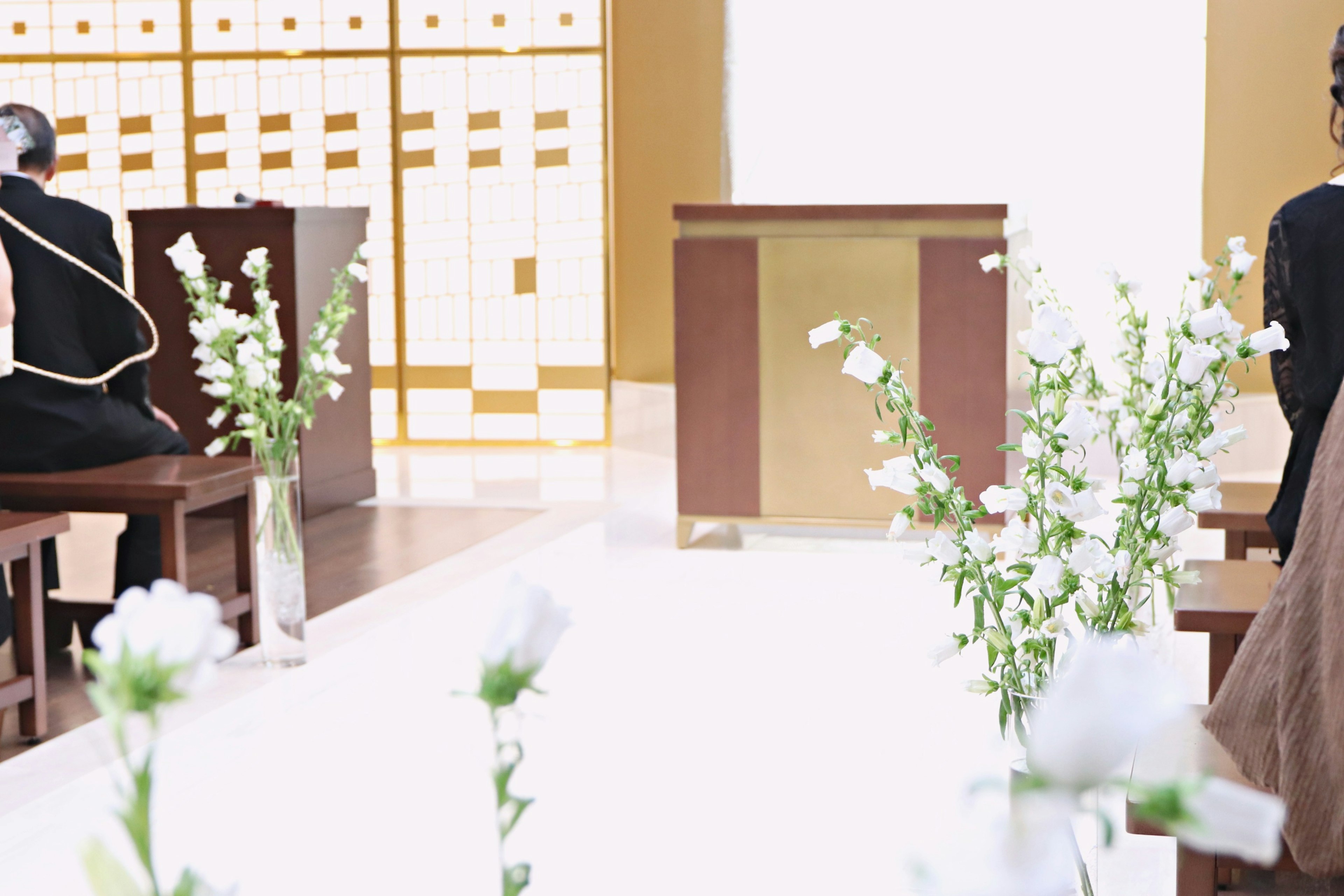 Interior de una iglesia serena con flores blancas dispuestas a lo largo del pasillo personas sentadas en el fondo tonos cálidos