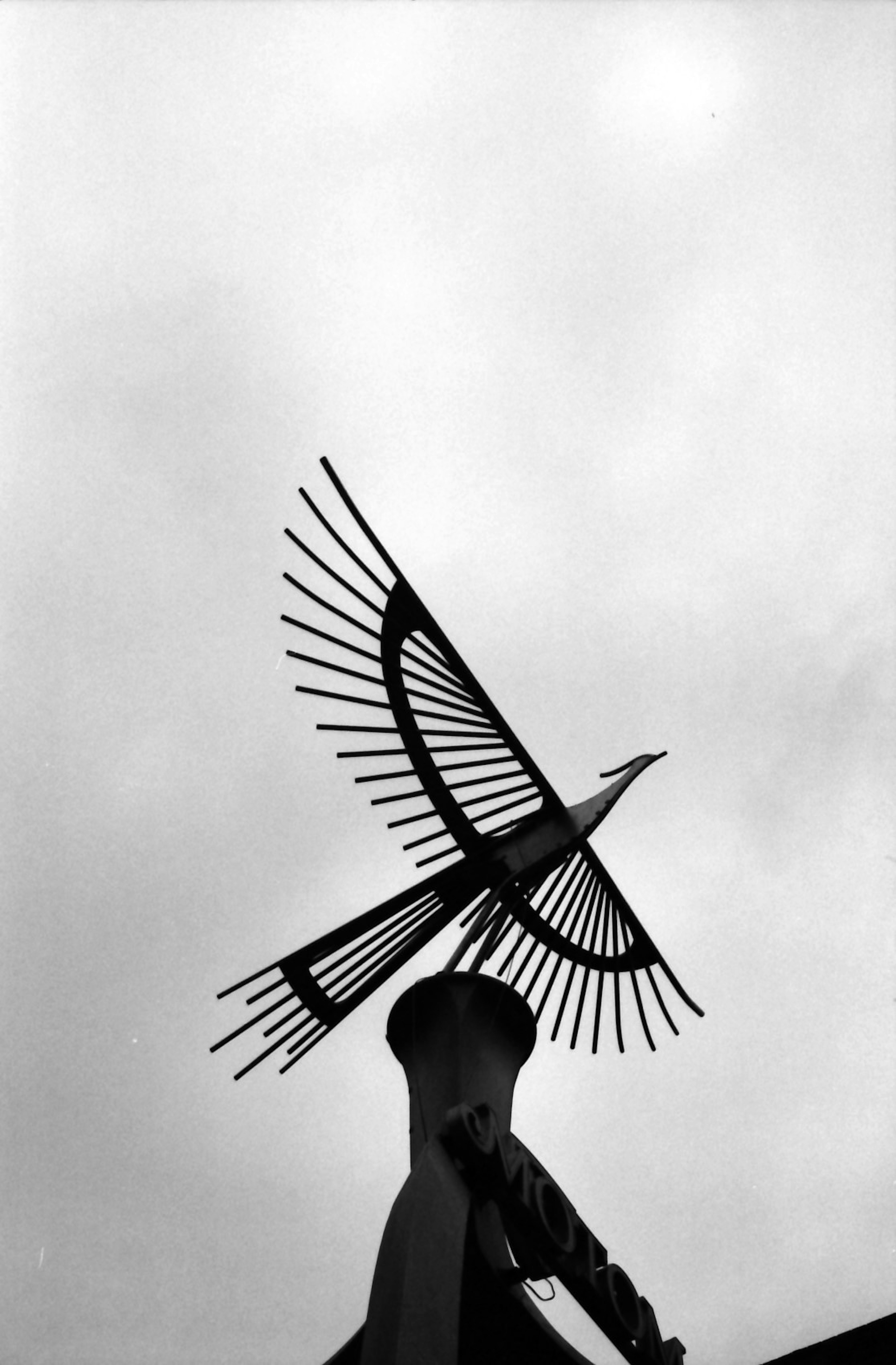 Bird sculpture against a cloudy sky with prominent sharp feathers