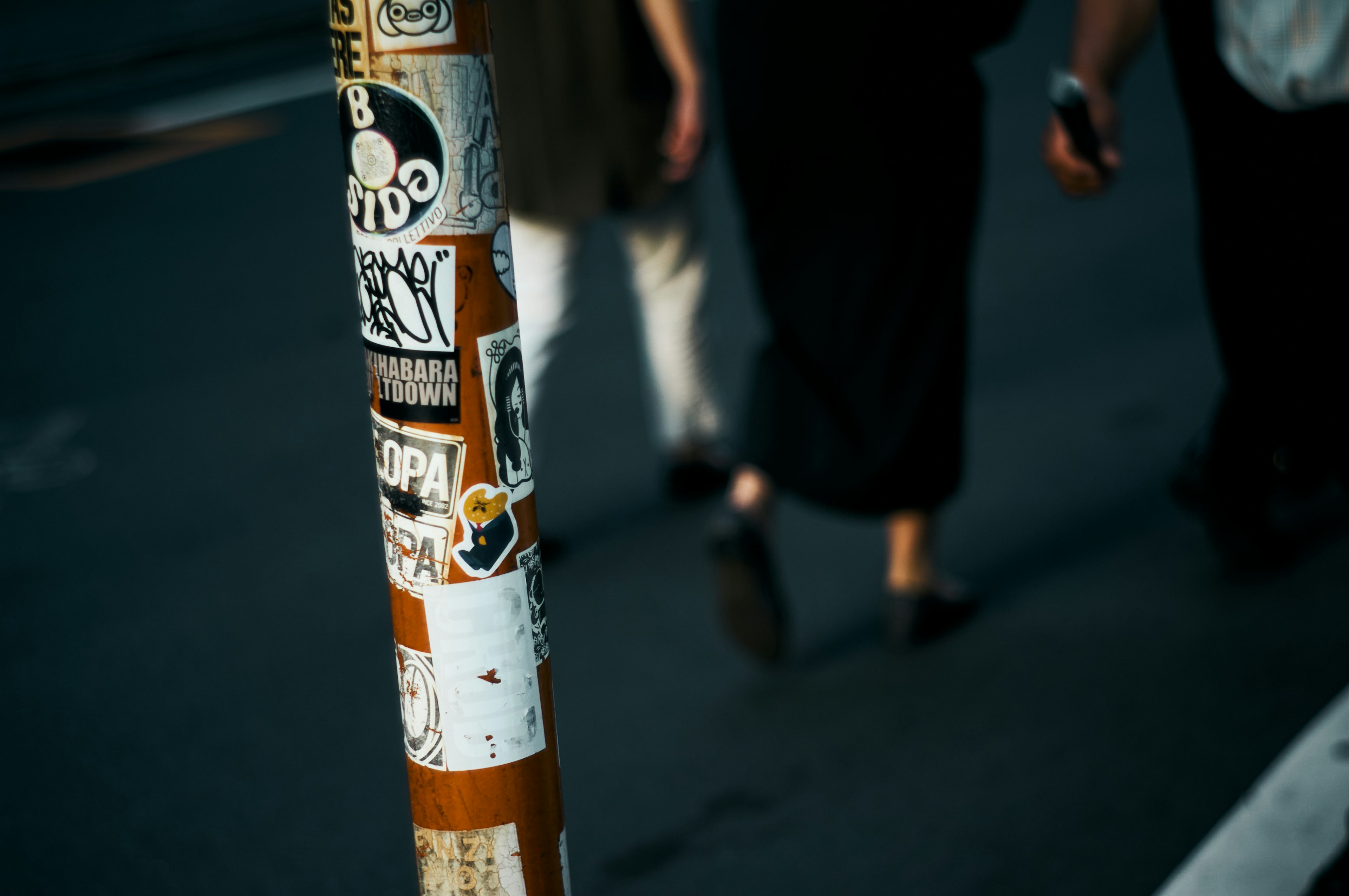 Un poste de calle cubierto de pegatinas con personas caminando al fondo