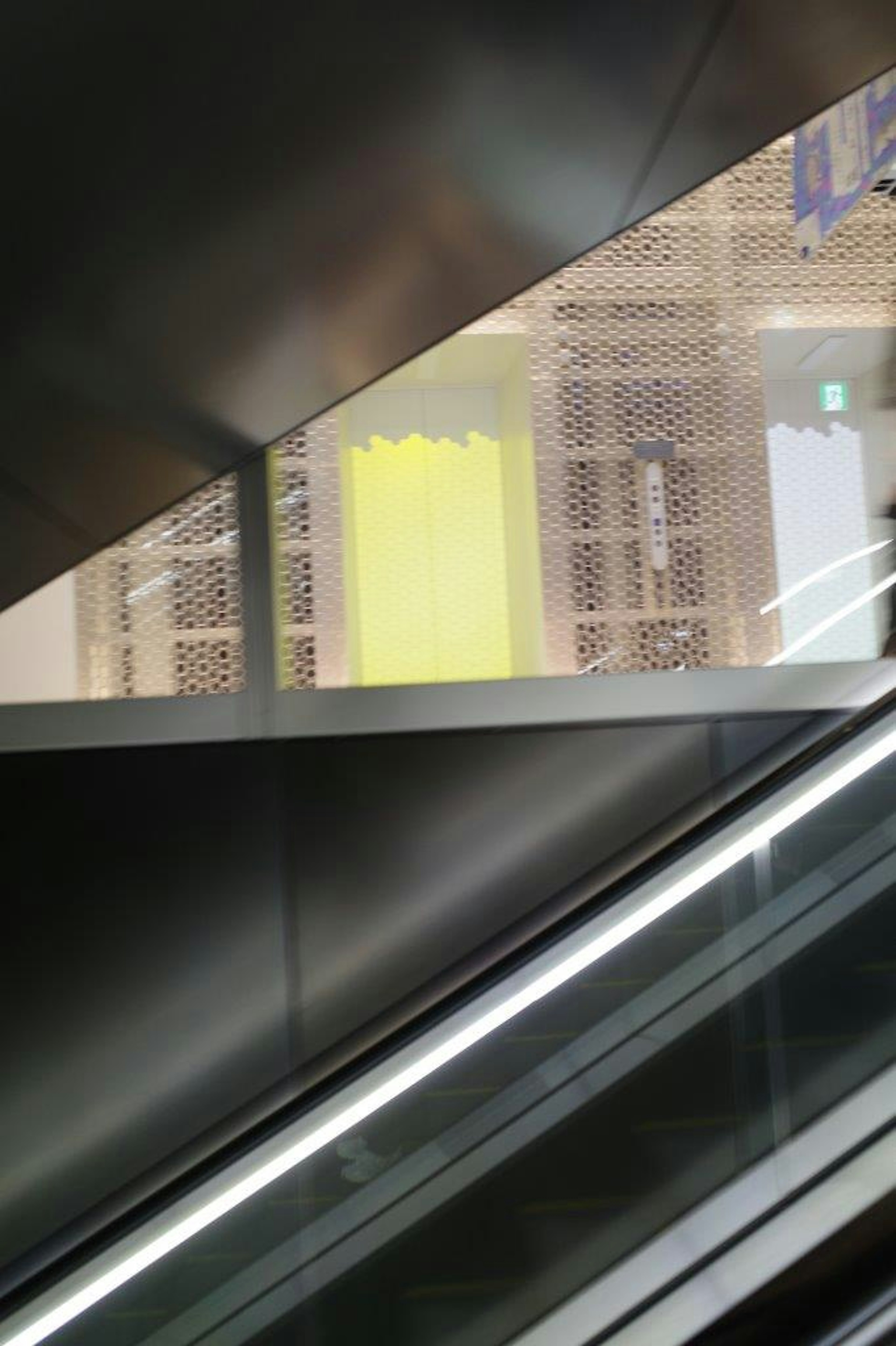 Vue d'un escalier roulant avec un mur transparent montrant une décoration jaune