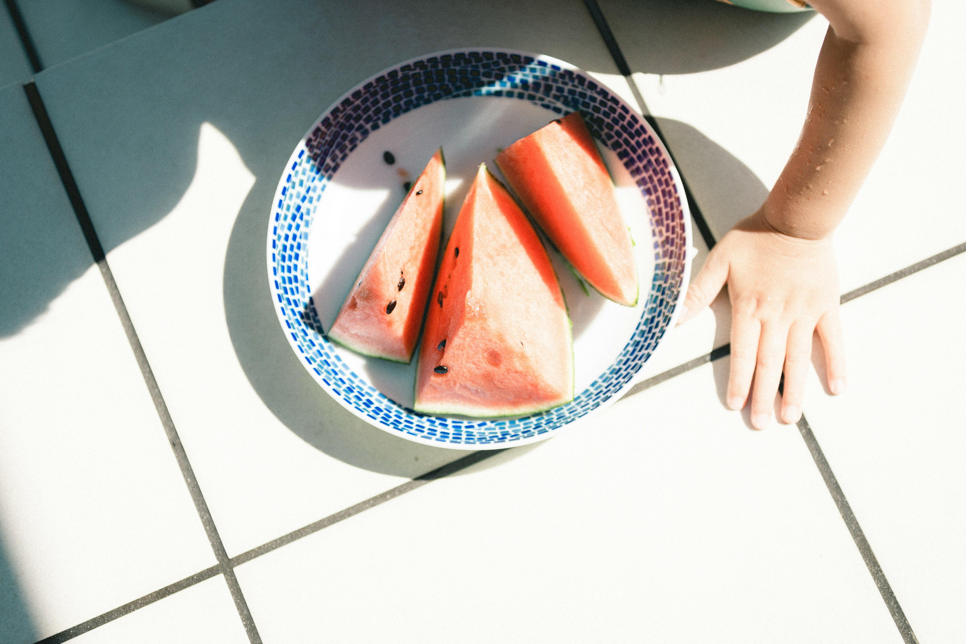 Slices of watermelon on a plate on white tiles with a child's hand