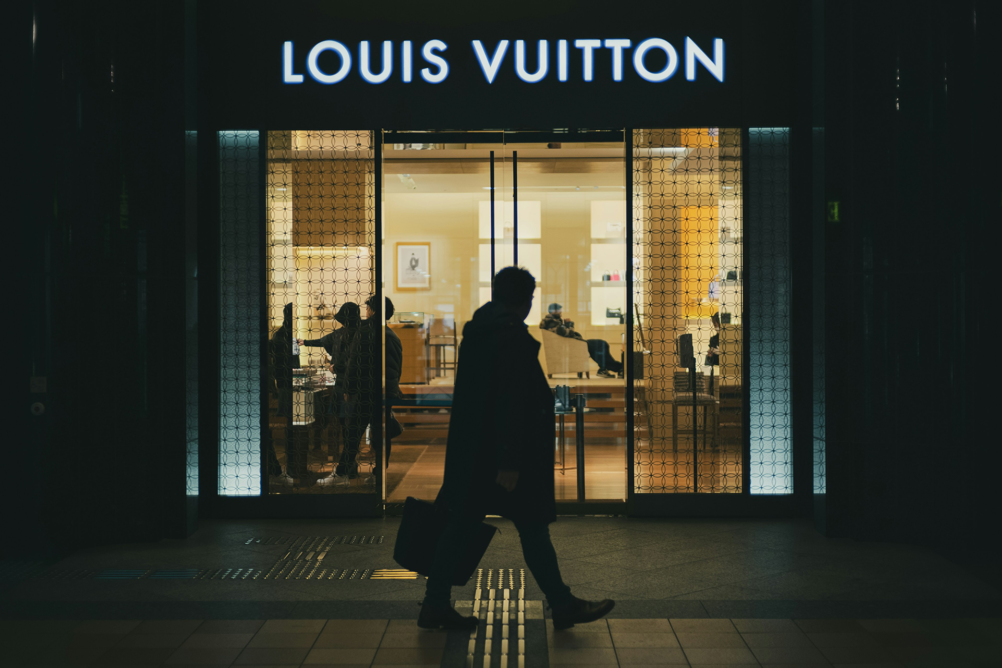 Silhouette de una persona caminando frente a una tienda Louis Vuitton con luces interiores